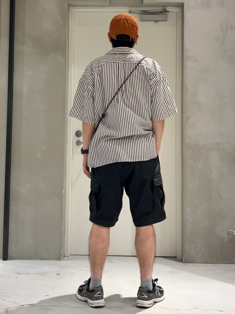 ブラック系のカーゴパンツ、ブラック系のショルダーバッグ、ベージュ系のスニーカーを着用したメンズの夏コーディネートの2枚目の写真