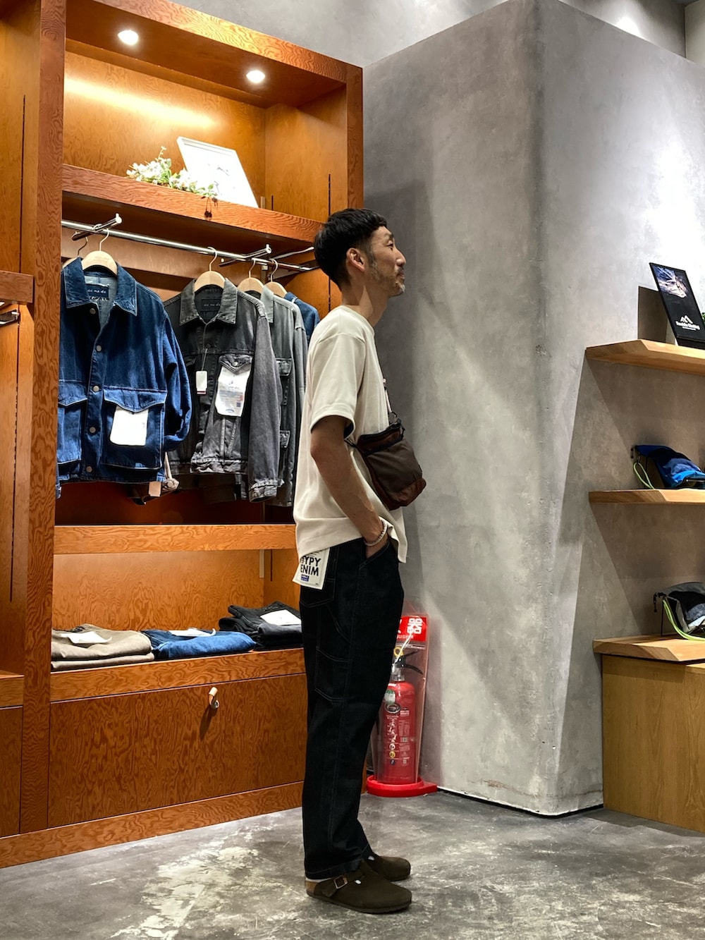 ブラック系のデニムパンツ、ブラウン系のショルダーバッグ、ホワイト系のTシャツ/カットソーを着用したメンズの夏コーディネートの2枚目の写真