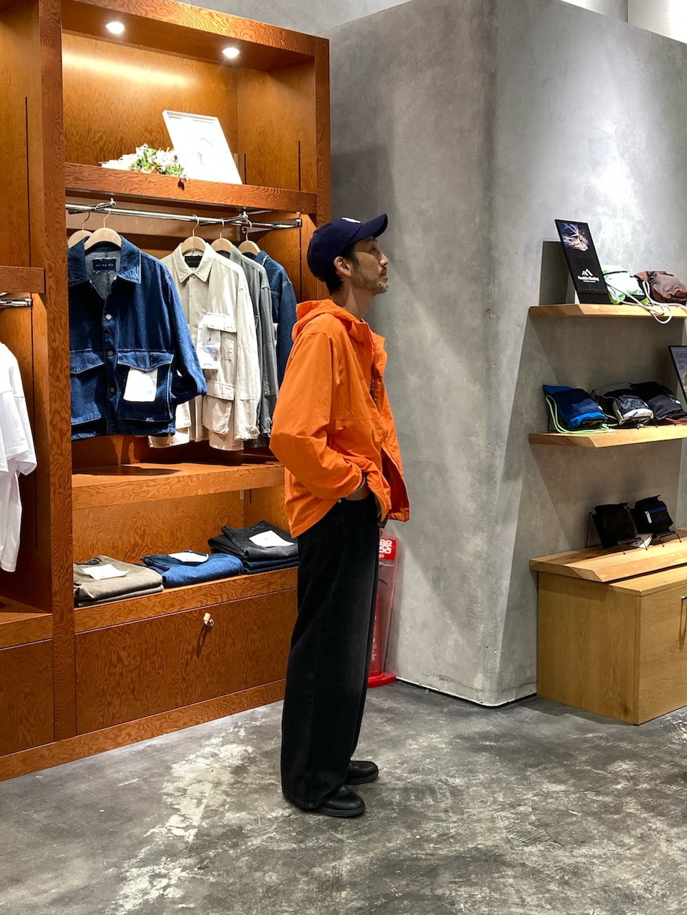 ブラック系のデニムパンツ、グレー系のTシャツ/カットソー、オレンジ系のマウンテンパーカーを着用したメンズの夏コーディネートの2枚目の写真