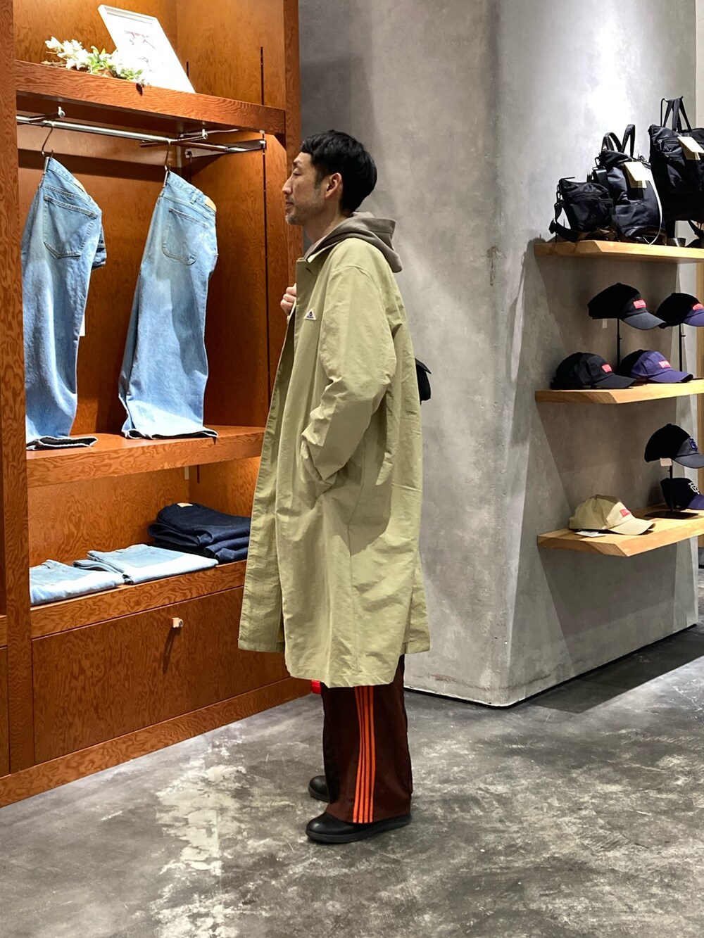 ベージュ系のステンカラーコート、ベージュ系のパーカー、ブラック系のショルダーバッグを着用したメンズの春コーディネートの2枚目の写真