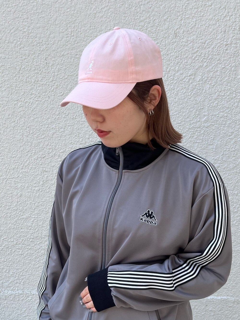 グレー系のジャージ、ピンク系のスニーカー、ピンク系のキャップを着用したレディースの春コーディネートの2枚目の写真