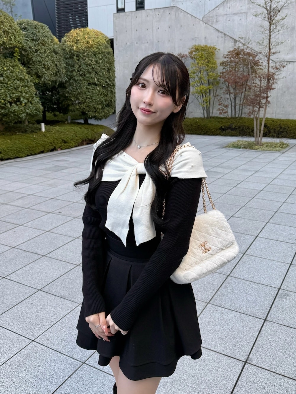 ブラック系のブーツ、ホワイト系のショルダーバッグ、ブラック系のスカートを着用したレディースの冬コーディネートの2枚目の写真