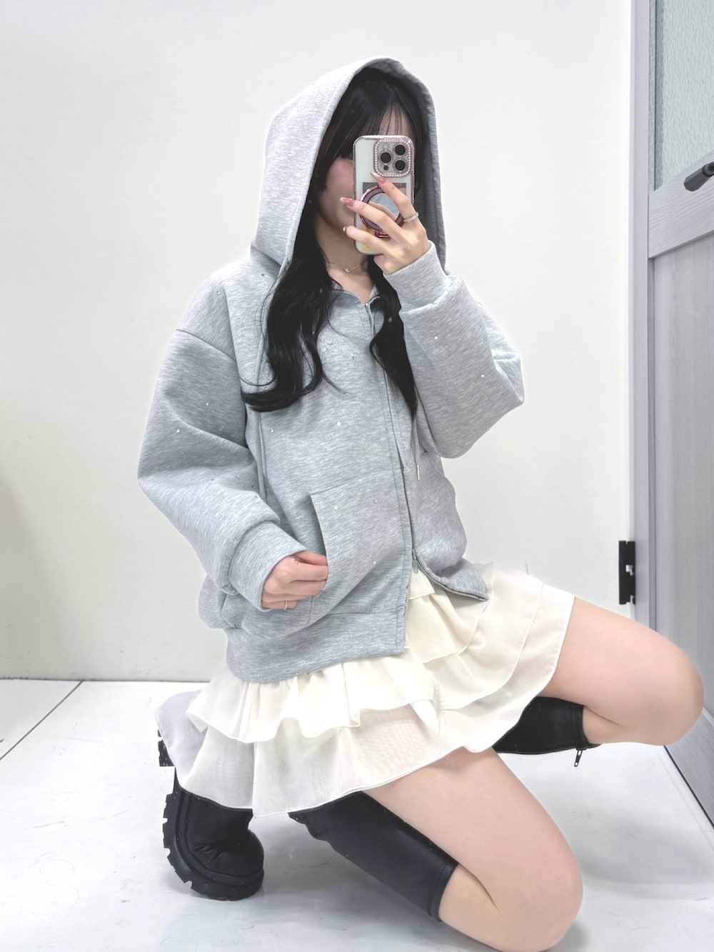 グレー系のパーカー、ホワイト系のスカート、ブラック系のブーツを着用したレディースの冬コーディネートの2枚目の写真