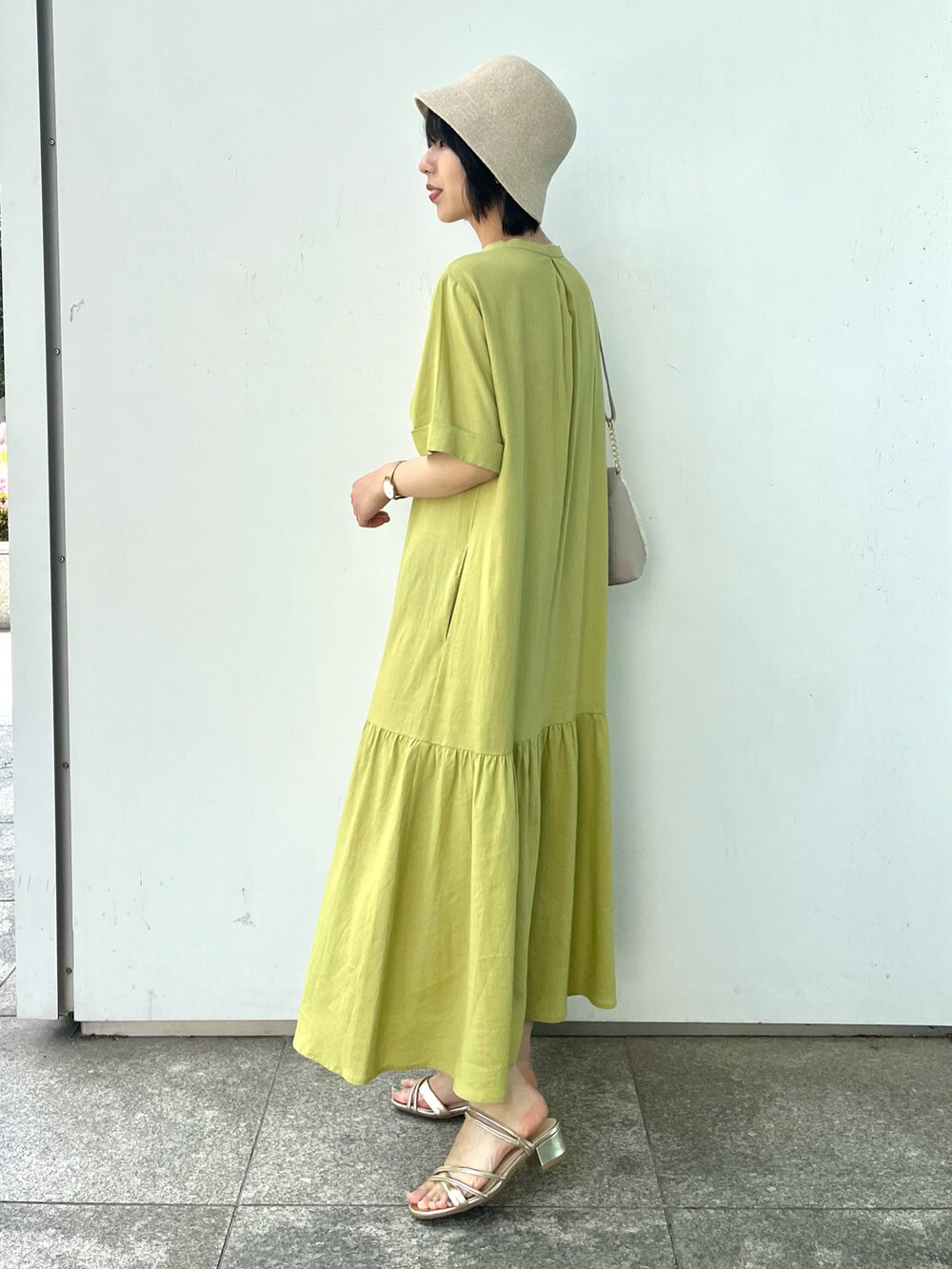 グレー系のショルダーバッグ、ゴールド系のサンダル、イエロー系のワンピースを着用したレディースの春コーディネートの2枚目の写真