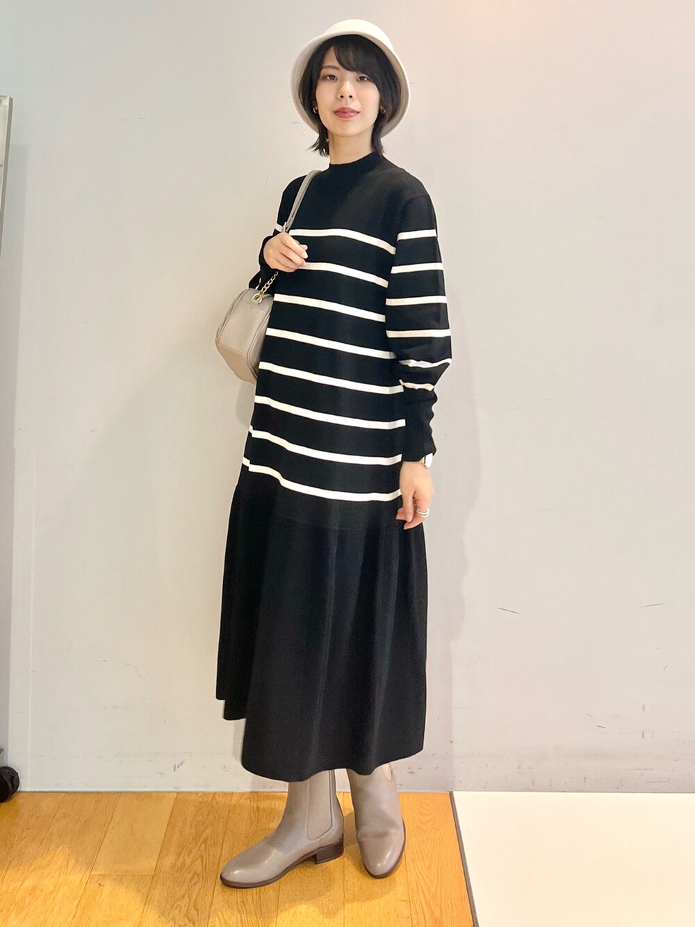 グレー系のブーツ、ホワイト系のワンピース、グレー系のショルダーバッグを着用したレディースの秋コーディネートの2枚目の写真