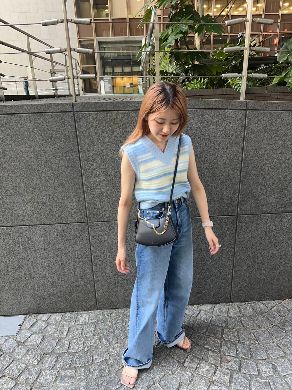 ベージュ系のサンダル、ブルー系のベスト、ブラック系のハンドバッグを着用したレディースの夏コーディネートの2枚目の写真