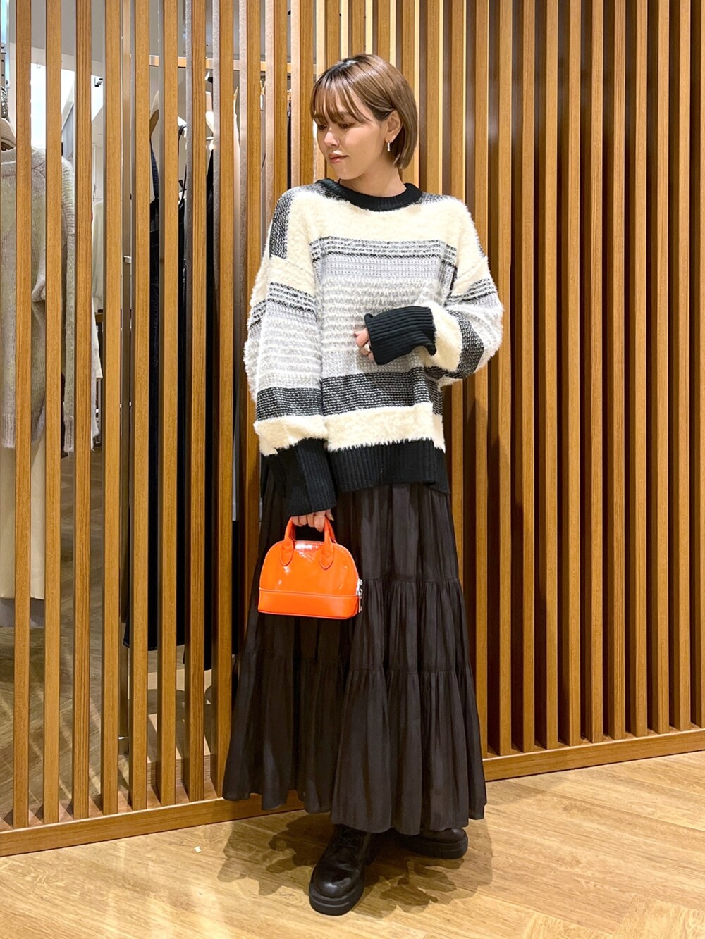 オレンジ系のショルダーバッグ、ブラック系のスカート、ブラック系のニット/セーターを着用したレディースの秋コーディネートの2枚目の写真