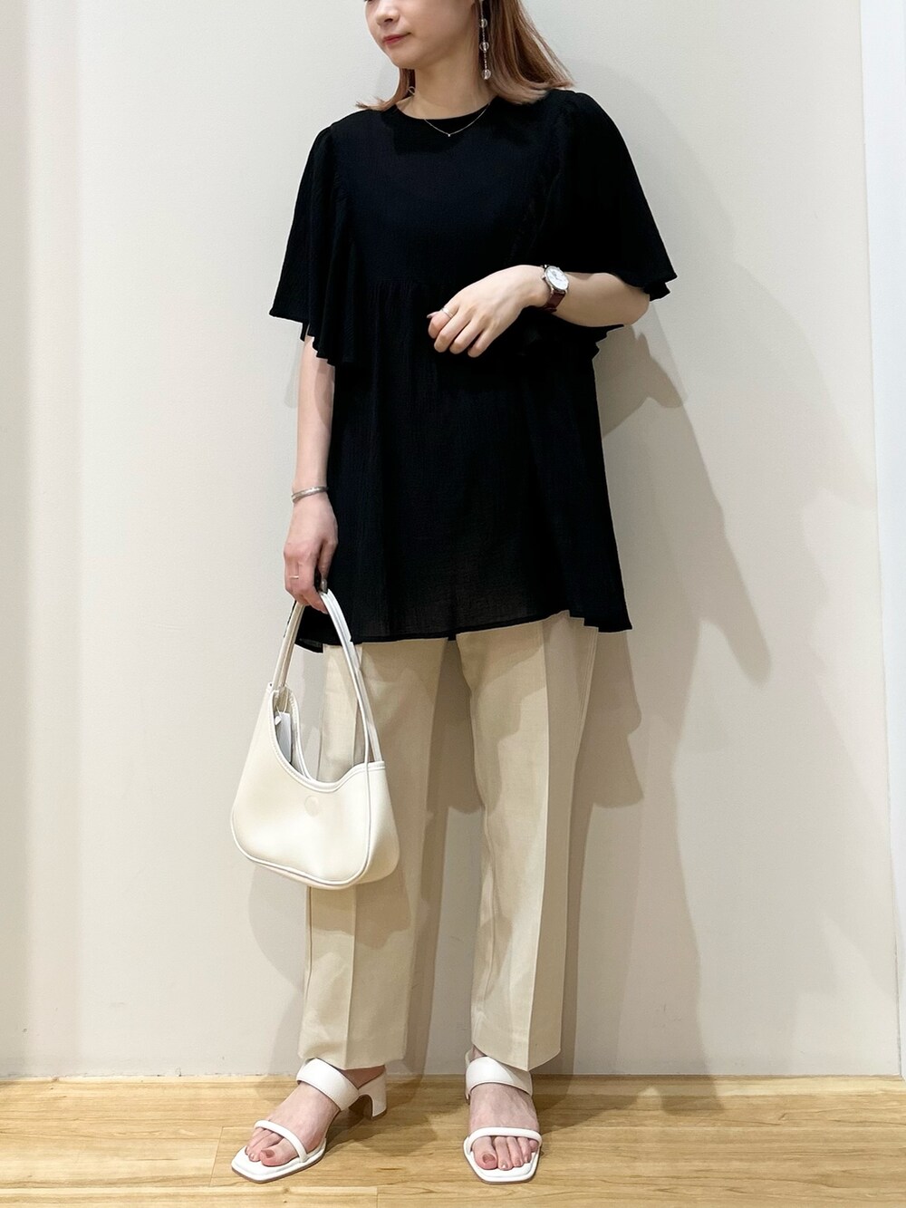 ホワイト系のハンドバッグ、ホワイト系のサンダル、ベージュ系のスラックスを着用したレディースの夏コーディネートの2枚目の写真