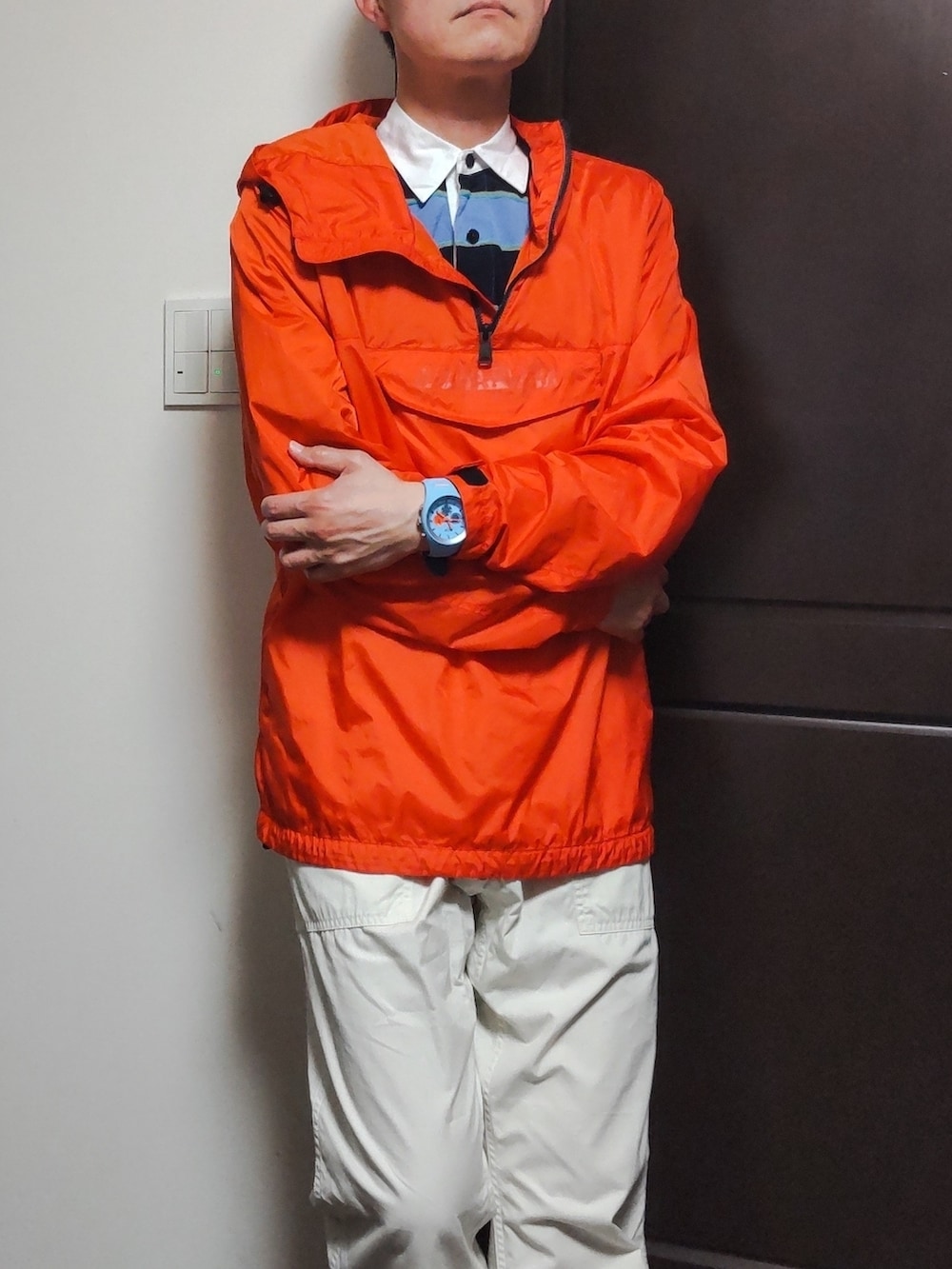 オレンジ系のマウンテンパーカー、ブルー系のポロシャツ、ホワイト系のパンツを着用したメンズの夏コーディネートの2枚目の写真