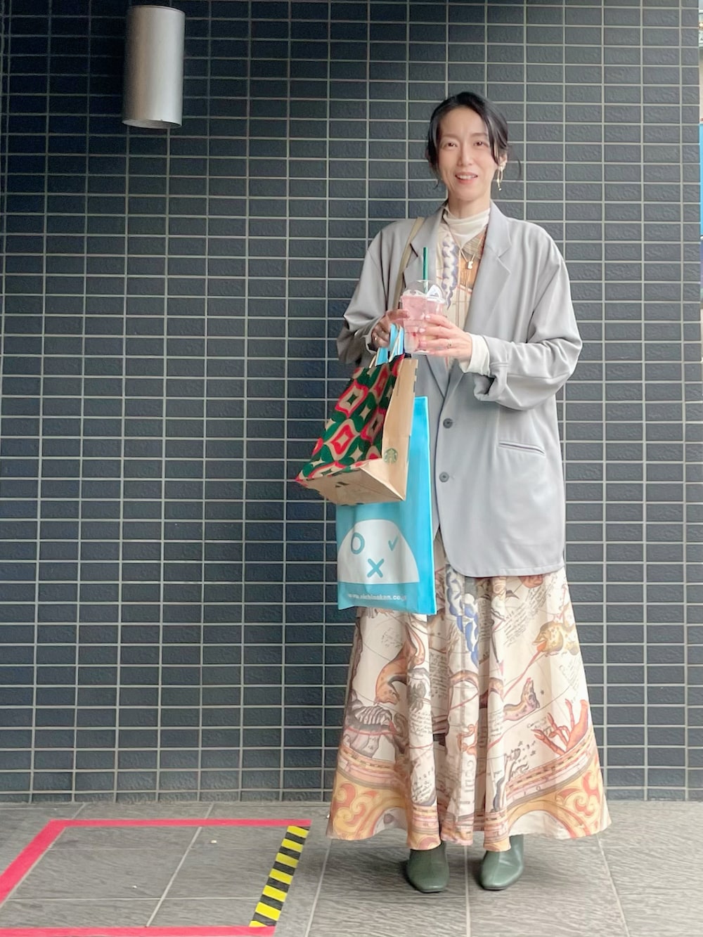 グレー系のテーラードジャケット、グリーン系のショルダーバッグ、イエロー系のワンピースを着用したレディースの秋コーディネートの2枚目の写真