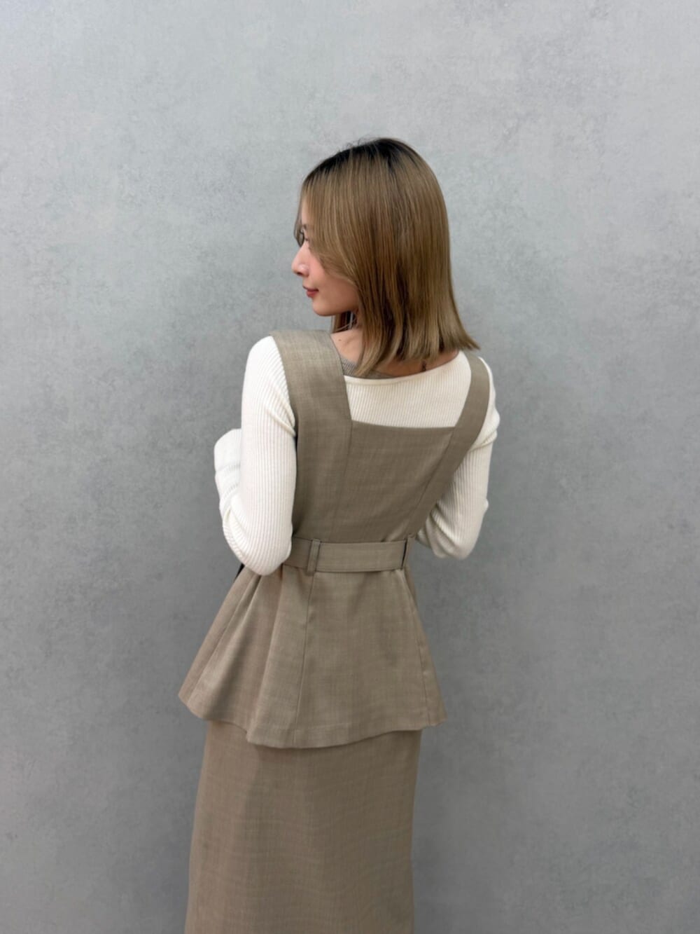 ベージュ系のジャンパースカート、ホワイト系のニット/セーター、ホワイト系のサンダルを着用したレディースの春コーディネートの5枚目の写真