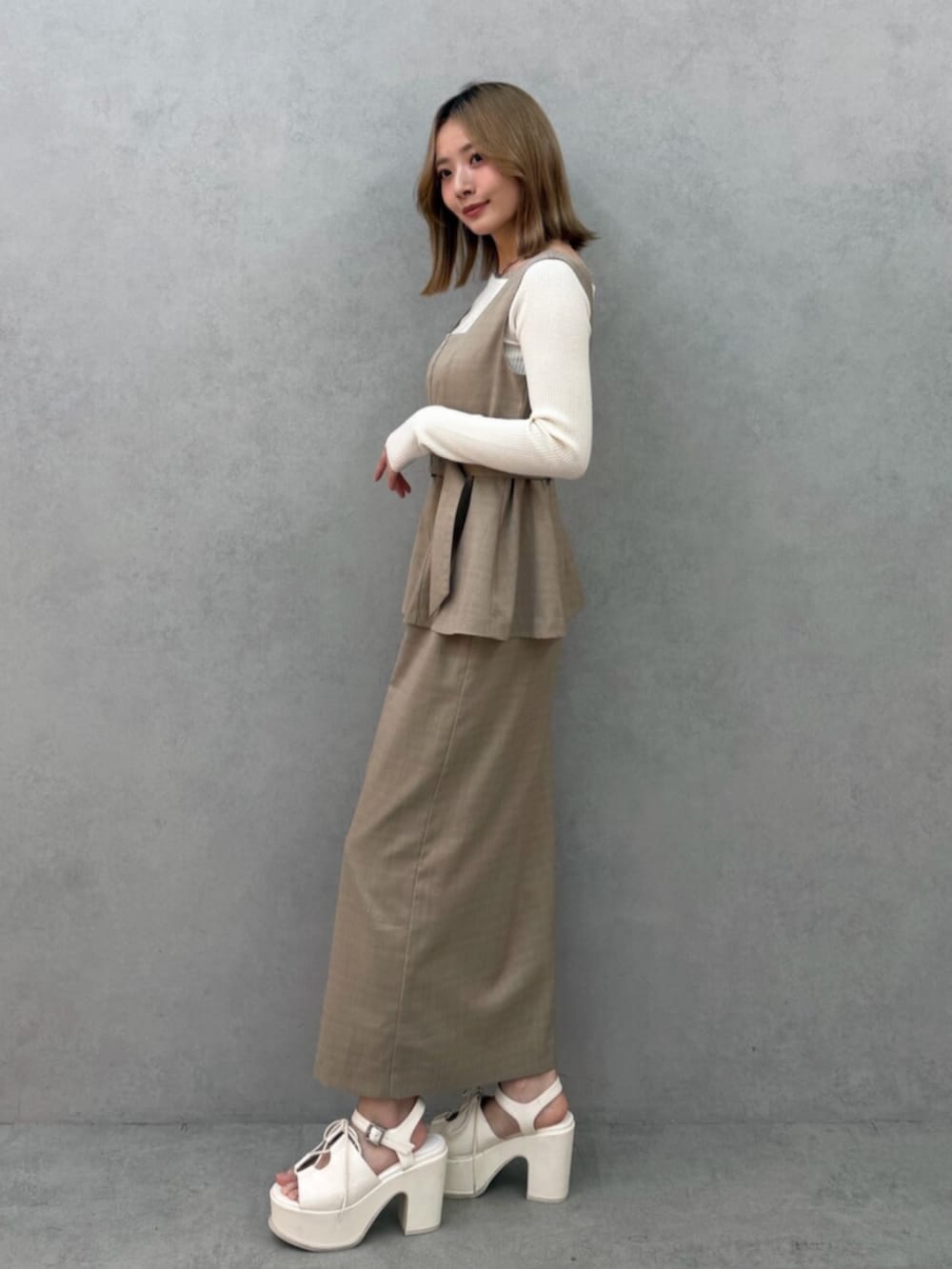 ベージュ系のジャンパースカート、ホワイト系のニット/セーター、ホワイト系のサンダルを着用したレディースの春コーディネートの3枚目の写真