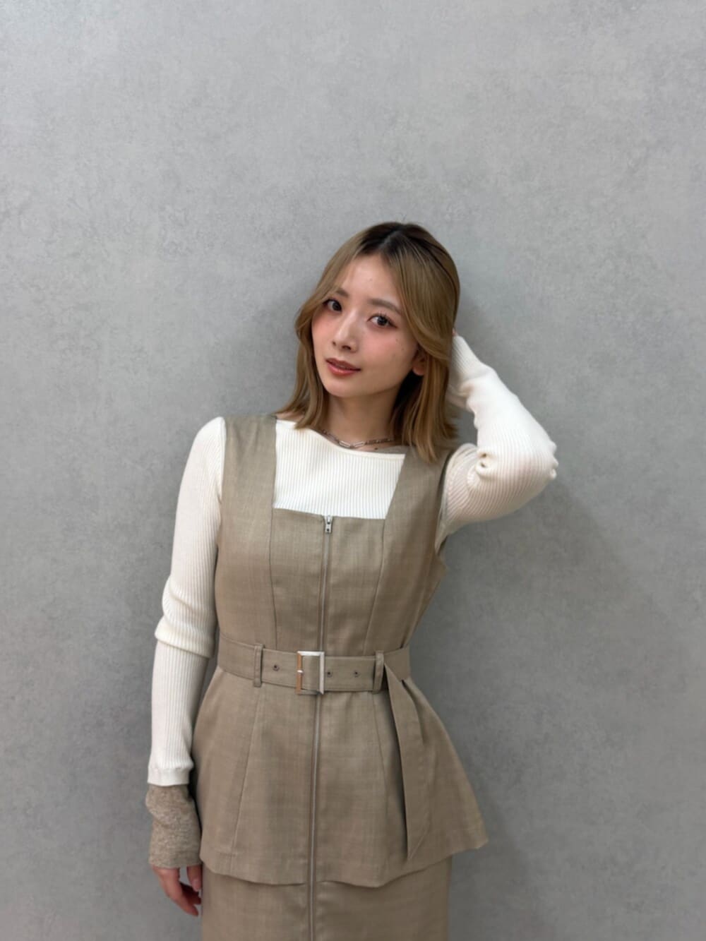 ベージュ系のジャンパースカート、ホワイト系のニット/セーター、ホワイト系のサンダルを着用したレディースの春コーディネートの2枚目の写真