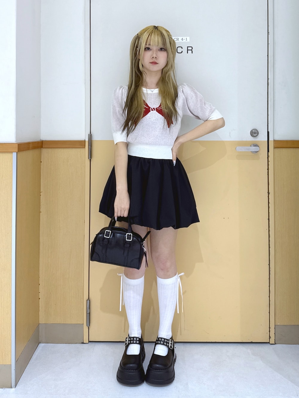 ブラック系のスカート、ホワイト系のトップス、ブラック系のショルダーバッグを着用したレディースの春コーディネートの2枚目の写真