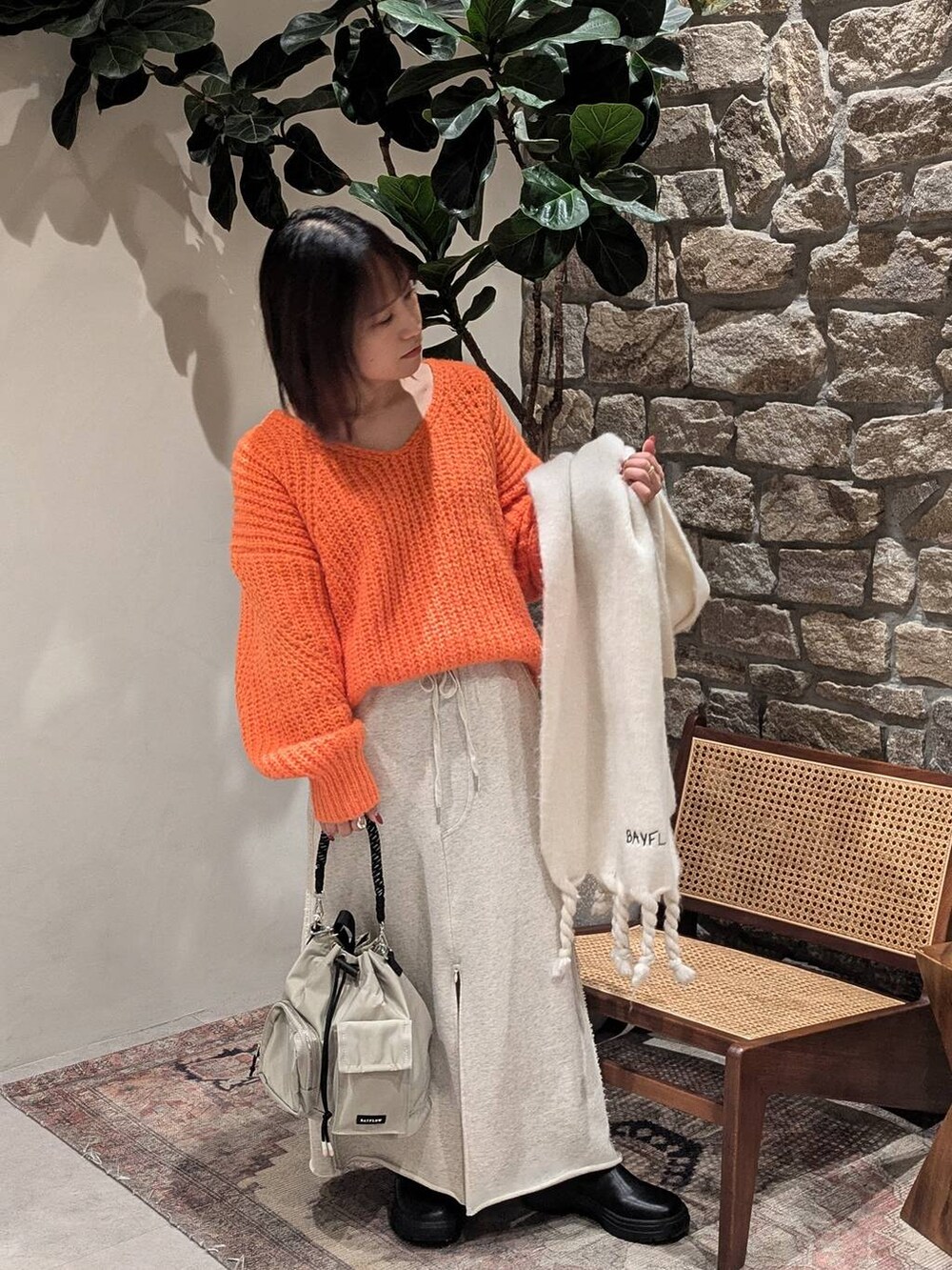 グレー系のショルダーバッグ、ブラック系のブーツ、オレンジ系のニット/セーターを着用したレディースの冬コーディネートの3枚目の写真