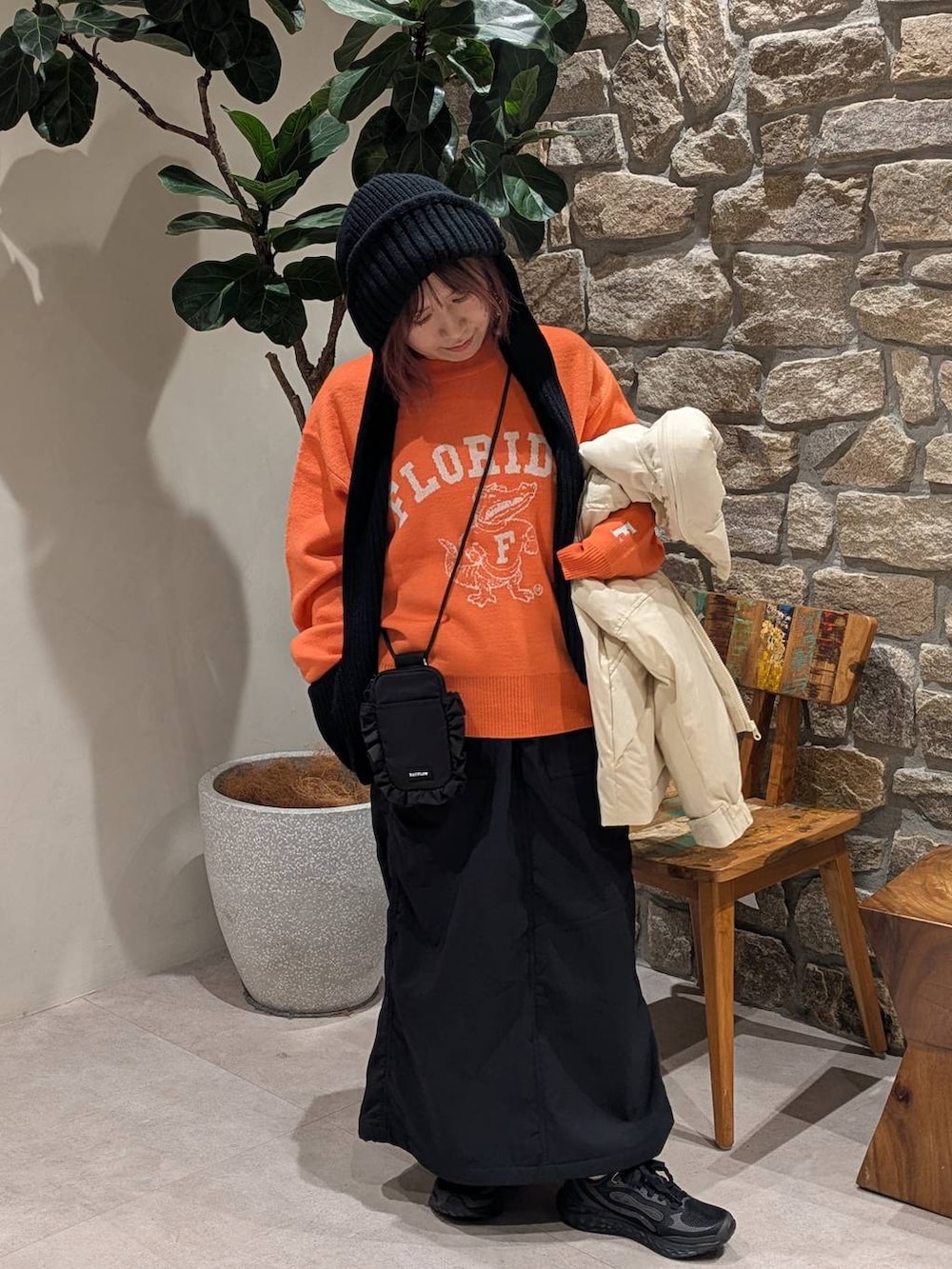 ブラック系のスカート、オレンジ系のニット/セーター、ホワイト系のダウンジャケット/コートを着用したレディースの冬コーディネートの4枚目の写真