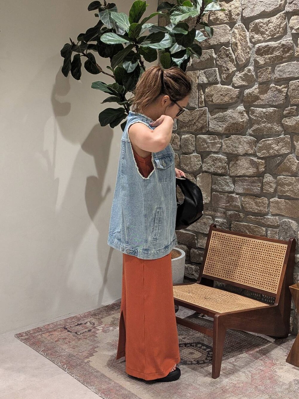 ブラック系のハンドバッグ、ブルー系のベスト、ブラック系のサンダルを着用したレディースの夏コーディネートの2枚目の写真