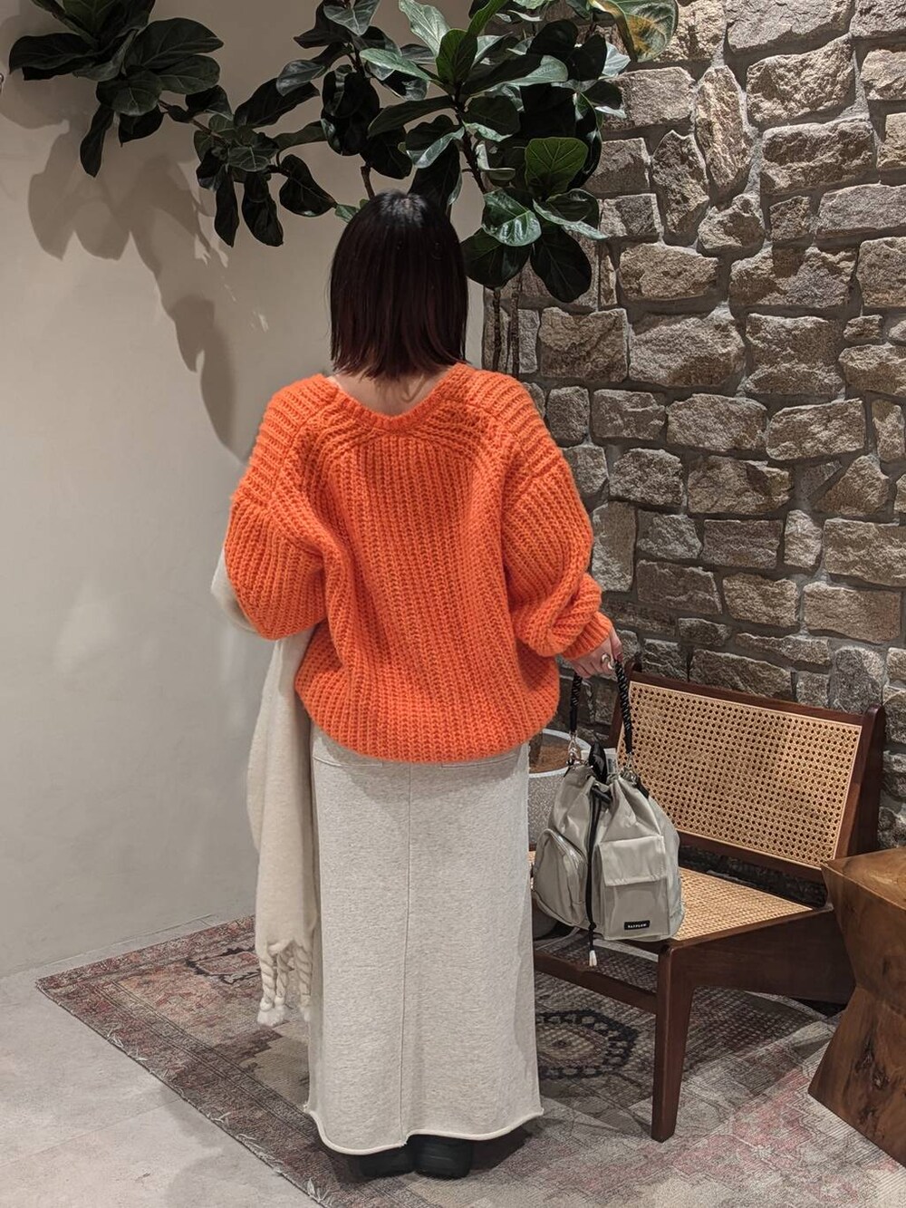 グレー系のショルダーバッグ、ブラック系のブーツ、オレンジ系のニット/セーターを着用したレディースの冬コーディネートの5枚目の写真