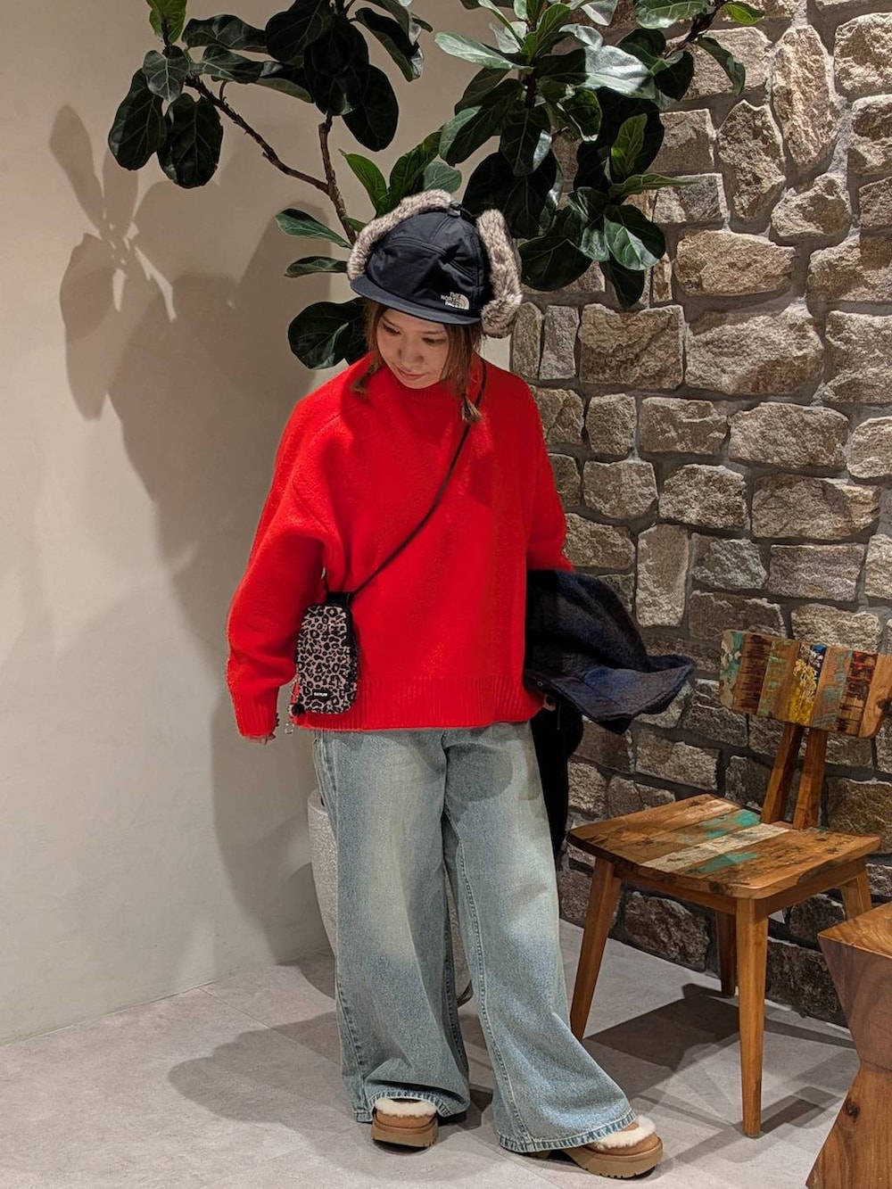 ブラウン系のショルダーバッグ、レッド系のニット/セーター、ブルー系のデニムパンツを着用したレディースの秋コーディネートの3枚目の写真