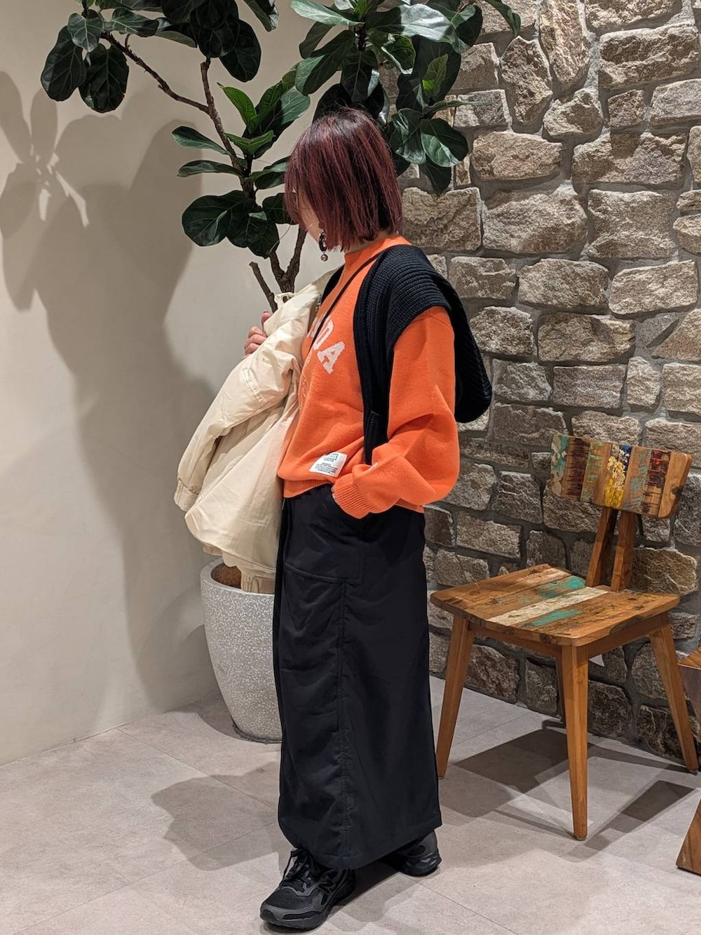 ブラック系のスカート、オレンジ系のニット/セーター、ホワイト系のダウンジャケット/コートを着用したレディースの冬コーディネートの5枚目の写真