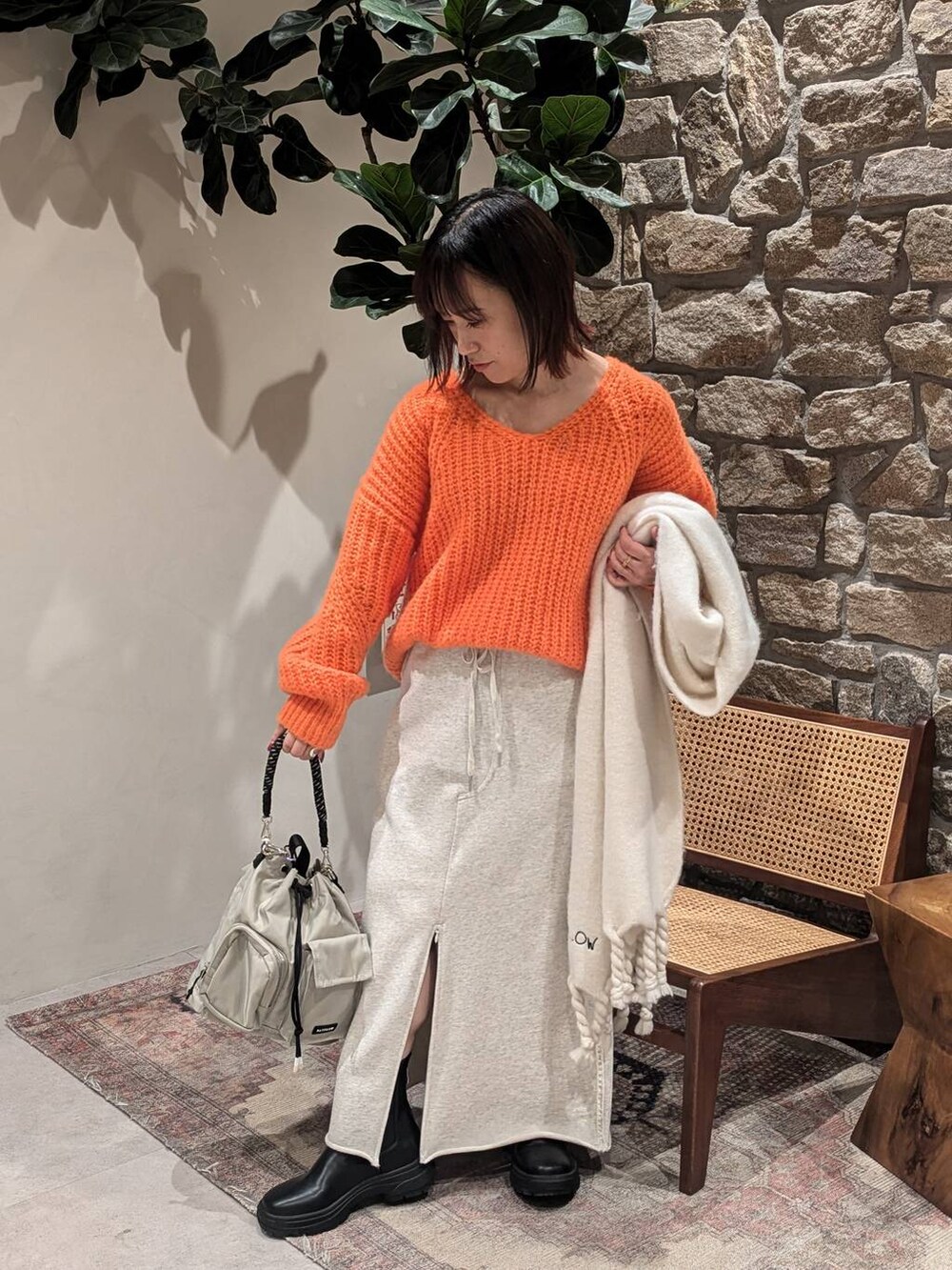 グレー系のショルダーバッグ、ブラック系のブーツ、オレンジ系のニット/セーターを着用したレディースの冬コーディネートの4枚目の写真