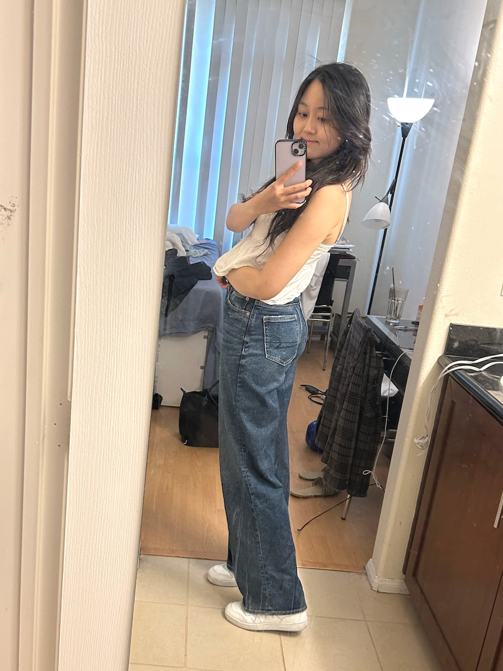 ブルー系のデニムパンツ、ホワイト系のスニーカー、ホワイト系のタンクトップを着用したレディースの春コーディネートの3枚目の写真