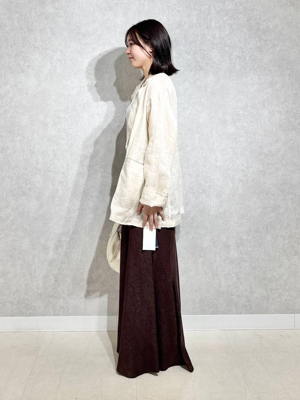 ホワイト系のハンドバッグ、ブラック系のパンプス、ブラウン系のスカートを着用したレディースの春コーディネートの2枚目の写真