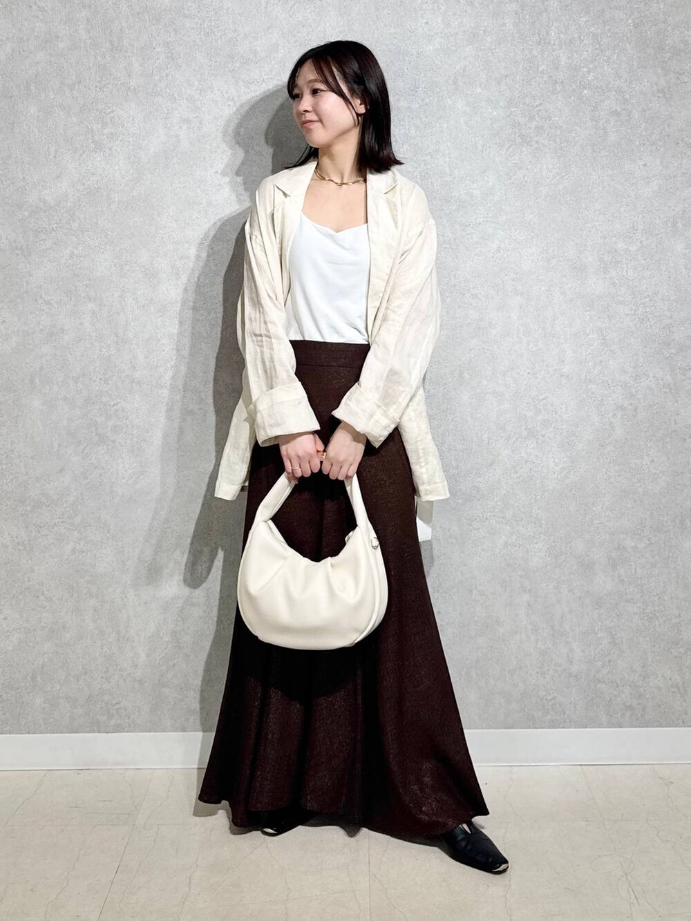 ホワイト系のハンドバッグ、ブラック系のパンプス、ブラウン系のスカートを着用したレディースの春コーディネートの5枚目の写真