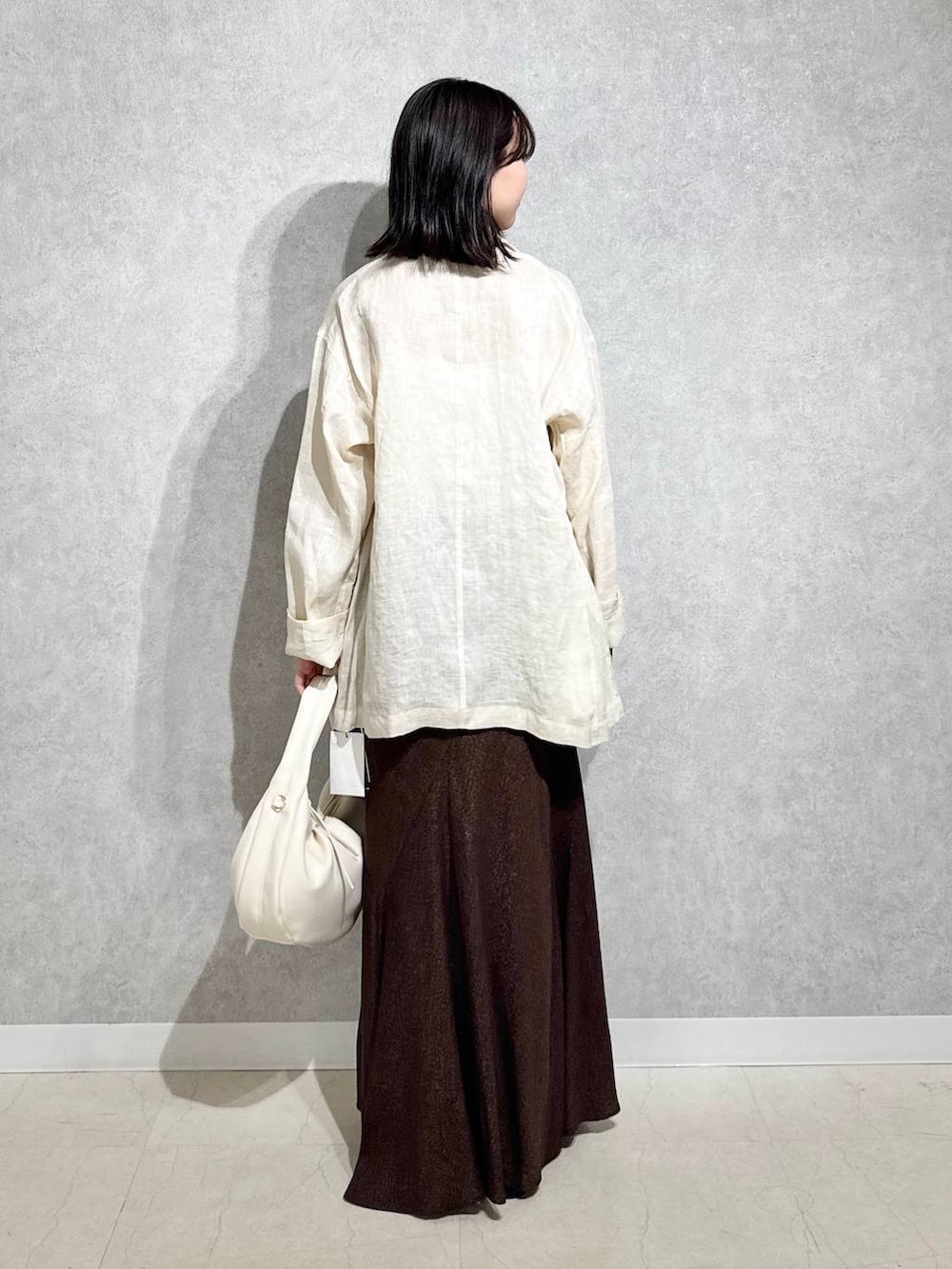 ホワイト系のハンドバッグ、ブラック系のパンプス、ブラウン系のスカートを着用したレディースの春コーディネートの3枚目の写真