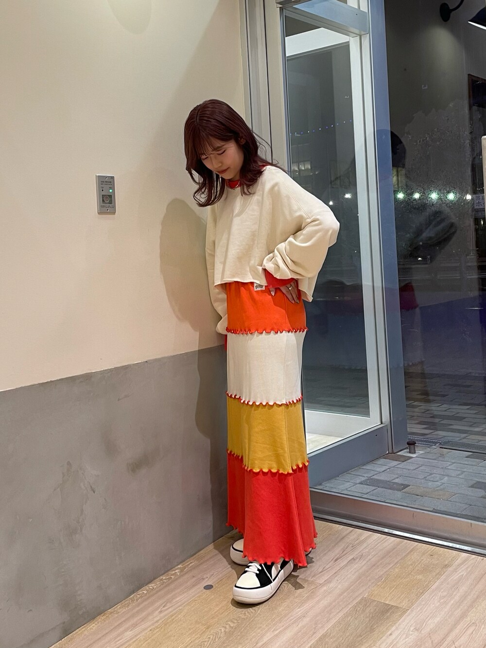 オレンジ系のTシャツ/カットソー、オレンジ系のスカート、ブラック系のスニーカーを着用したレディースの春コーディネートの2枚目の写真