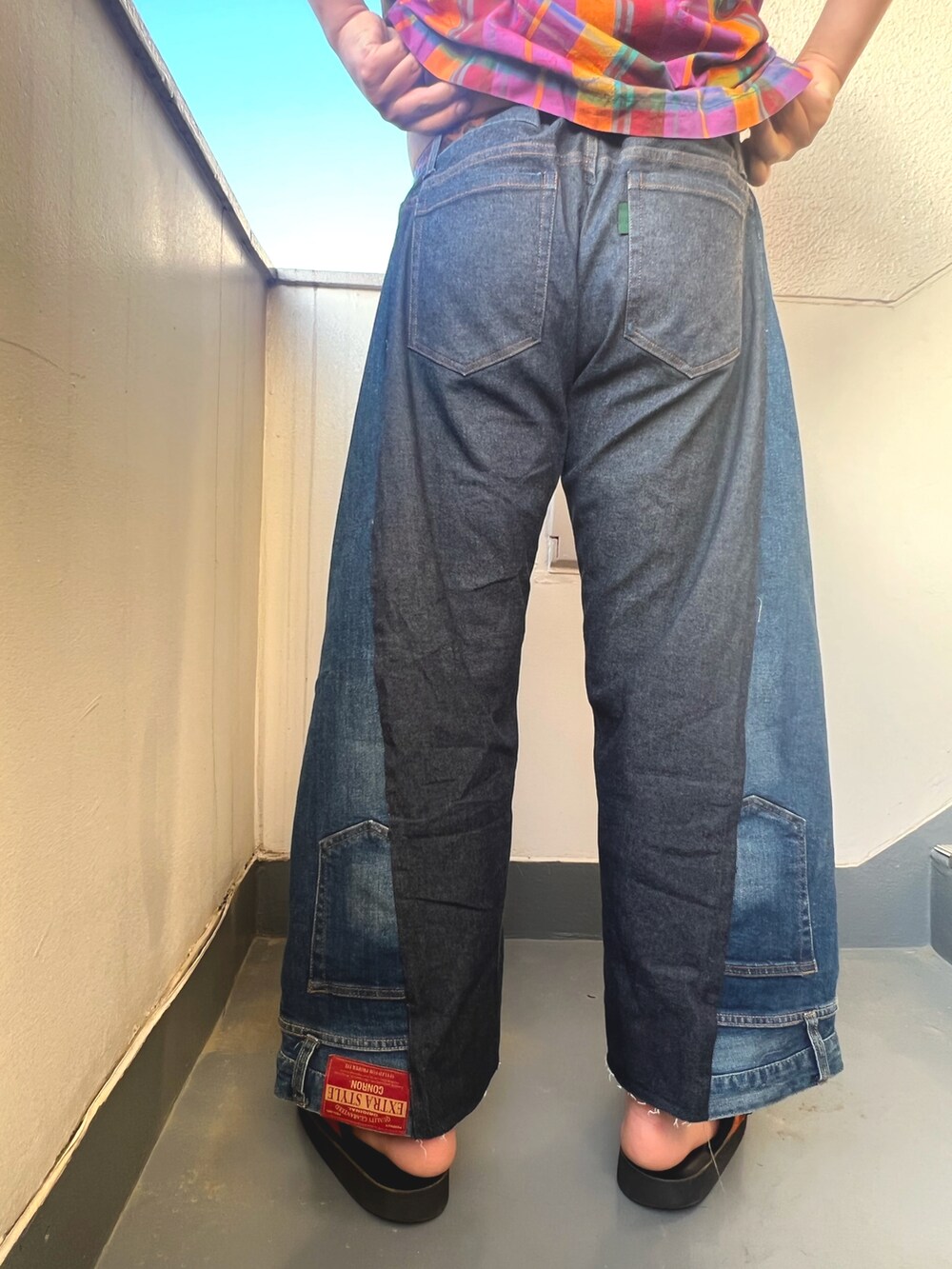 レッド系のトップス、ブルー系のデニムパンツ、オレンジ系のサンダルを着用したメンズの春コーディネートの3枚目の写真