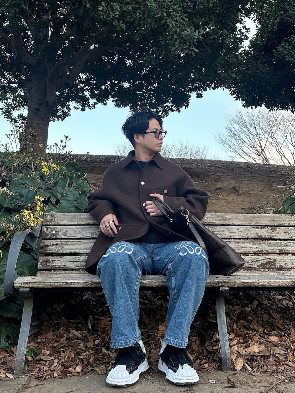 ブラウン系のカバーオール、ブラウン系のトートバッグ、ブルー系のデニムパンツを着用したメンズの冬コーディネートの2枚目の写真