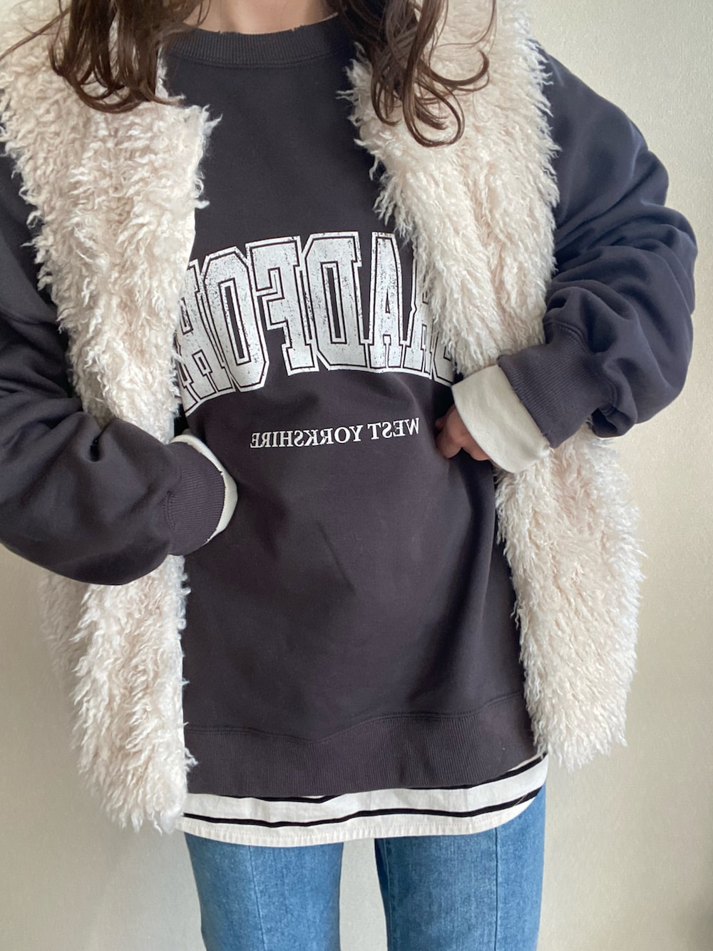 グレー系のスウェット、ホワイト系のベスト、ブルー系のデニムパンツを着用したレディースの冬コーディネートの2枚目の写真