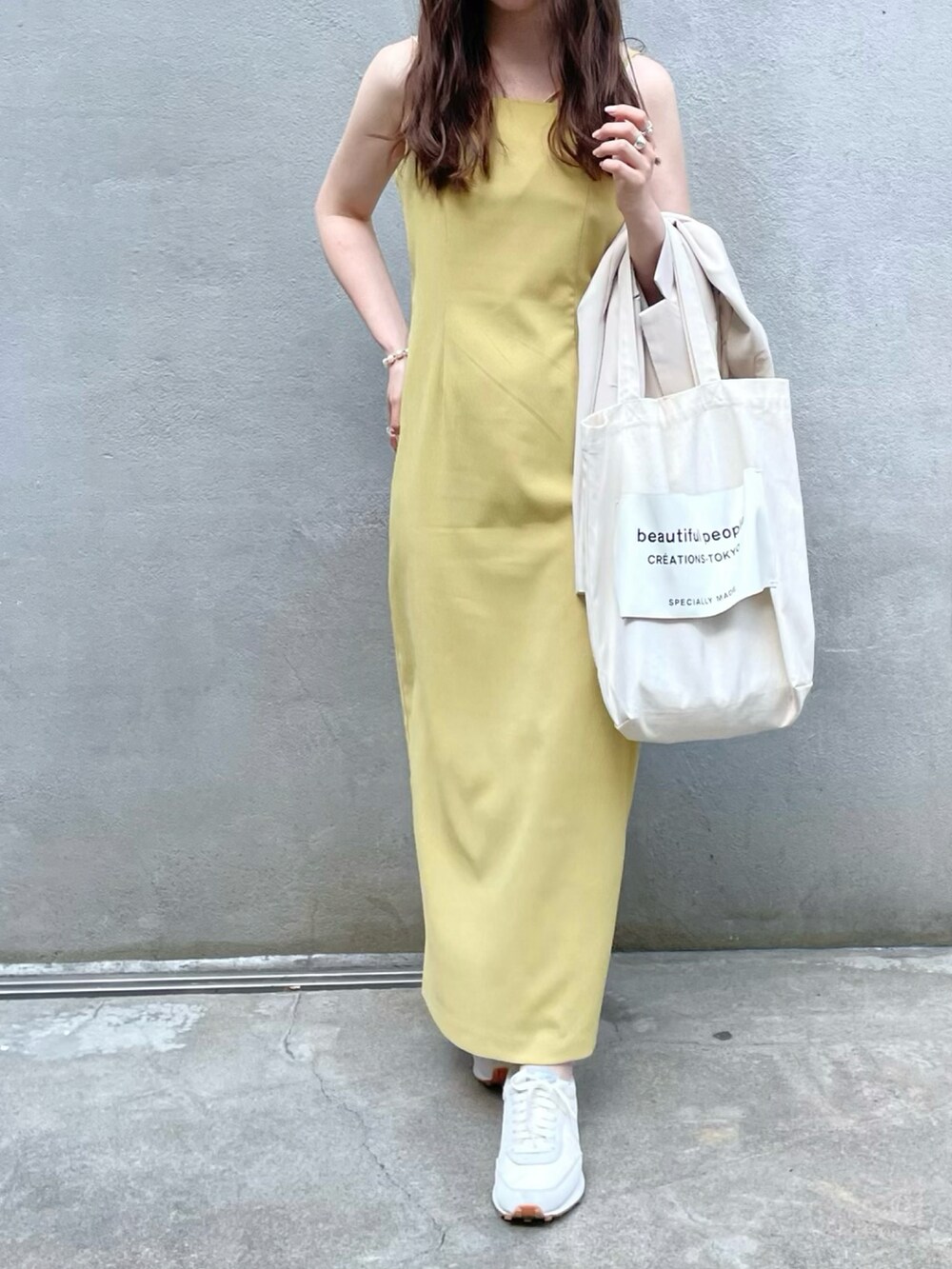 ホワイト系のトートバッグ、イエロー系のワンピース、ホワイト系のスニーカーを着用したレディースの夏コーディネートの2枚目の写真