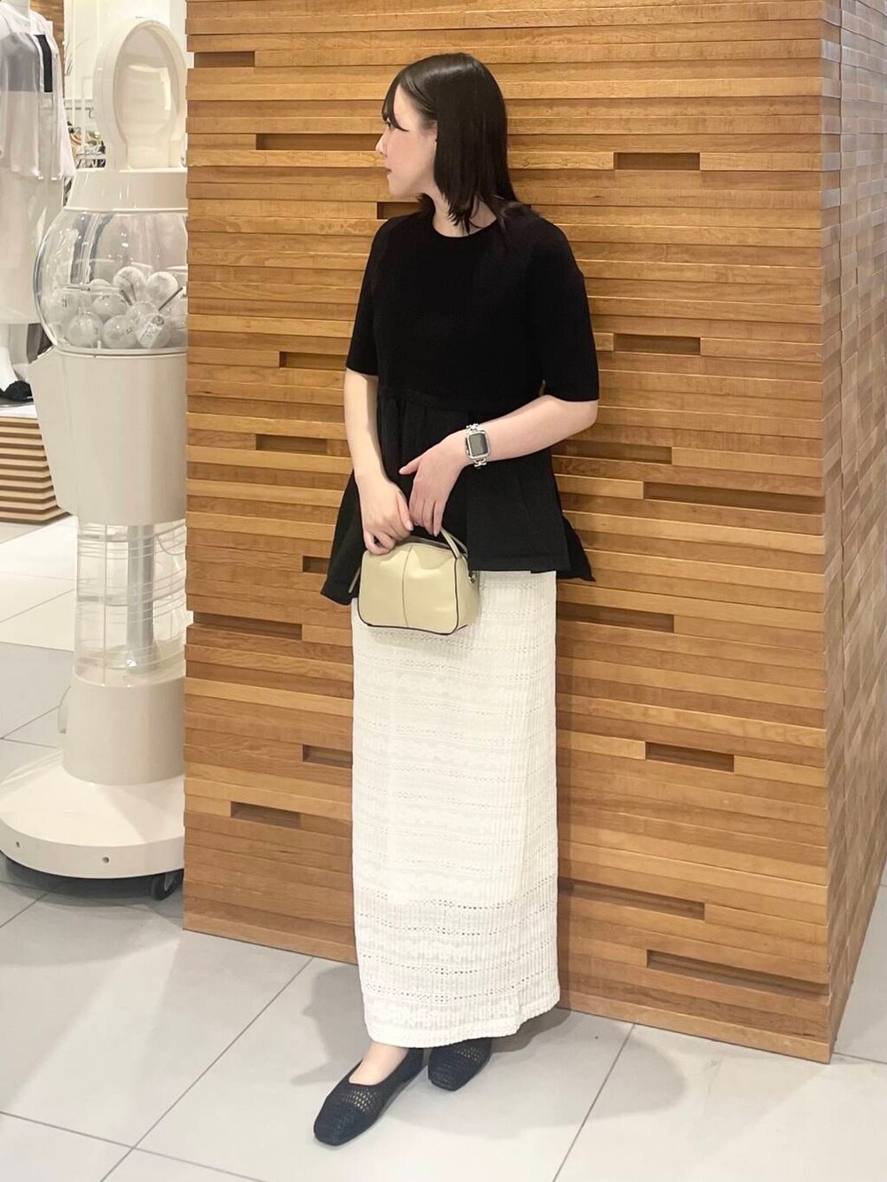 ベージュ系のハンドバッグ、ホワイト系のスカート、ブラック系のニット/セーターを着用したレディースの春コーディネートの2枚目の写真