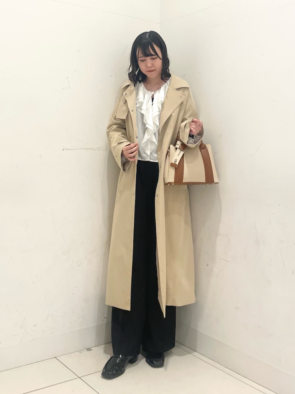 ブラック系のローファー、ブラック系のスラックス、ベージュ系のトレンチコートを着用したレディースの春コーディネートの2枚目の写真