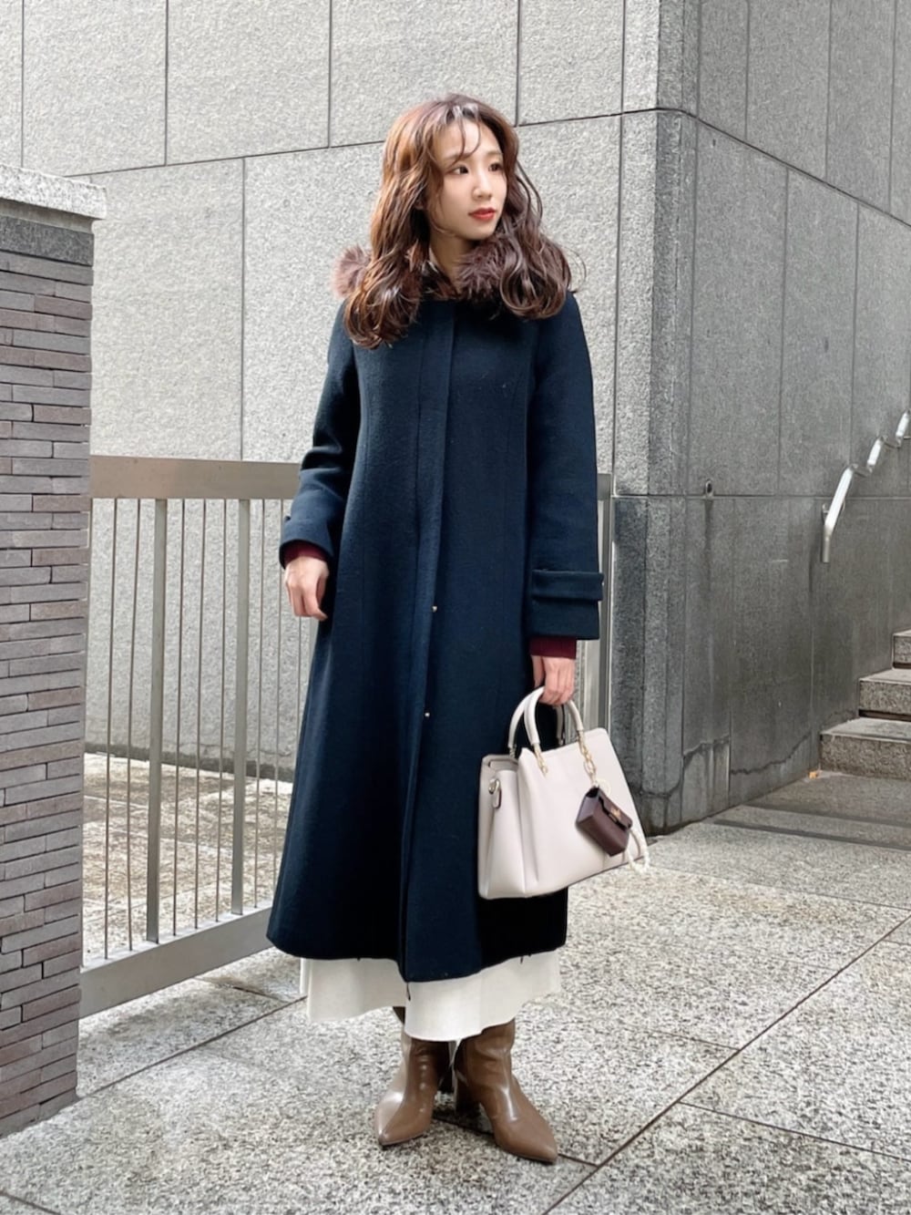 ブラウン系のブーツ、ブラック系のステンカラーコート、レッド系のワンピースを着用したレディースの冬コーディネートの3枚目の写真