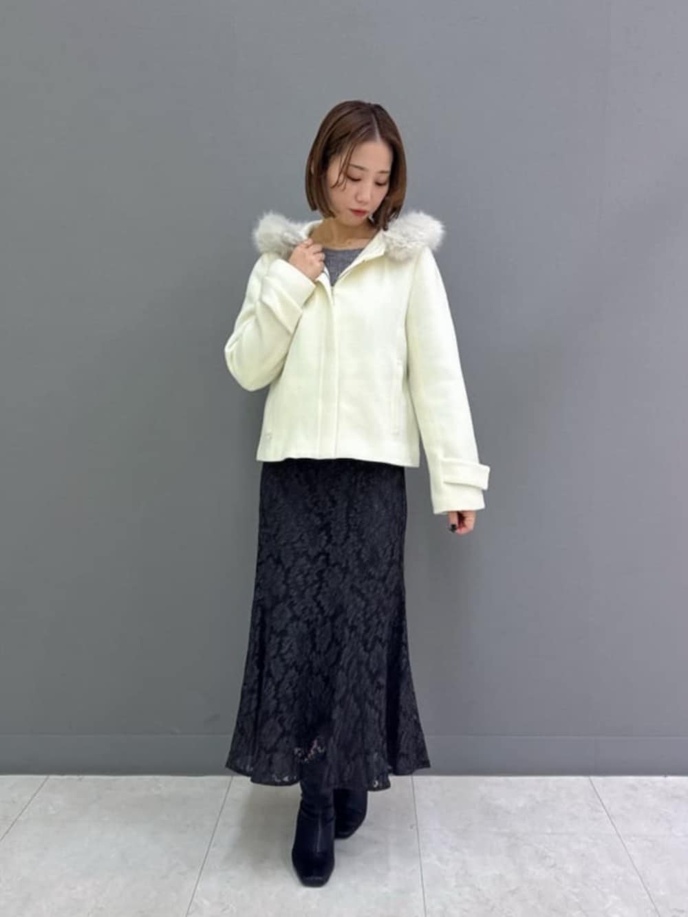 ホワイト系のブルゾン、グレー系のニット/セーター、グレー系のスカートを着用したレディースの冬コーディネートの2枚目の写真