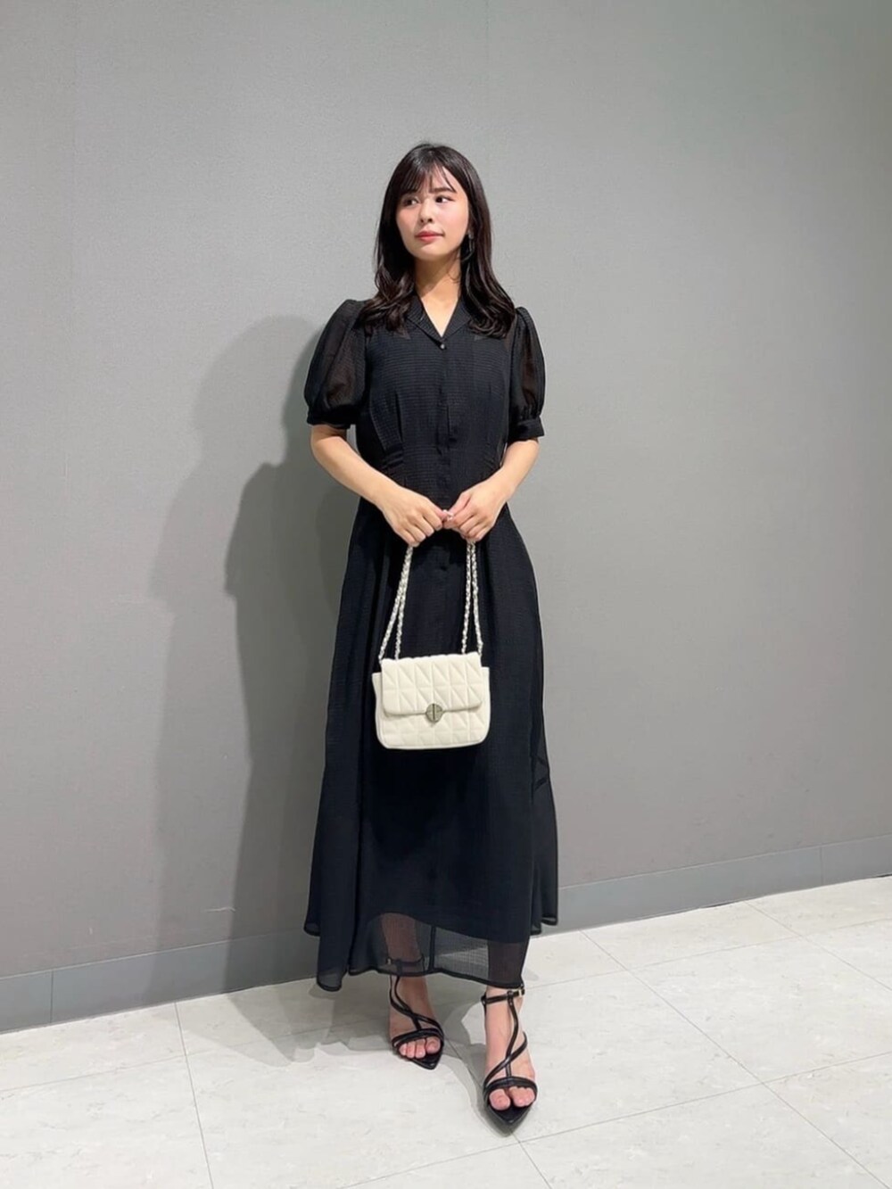 ホワイト系のショルダーバッグ、ブラック系のパンプス、ブラック系のワンピースを着用したレディースの夏コーディネートの2枚目の写真