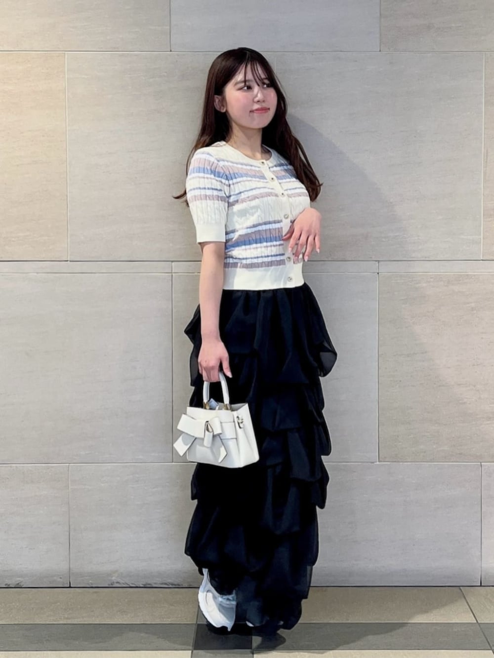 ホワイト系のショルダーバッグ、ホワイト系のカーディガン/ボレロ、ブラック系のスカートを着用したレディースの春コーディネートの2枚目の写真