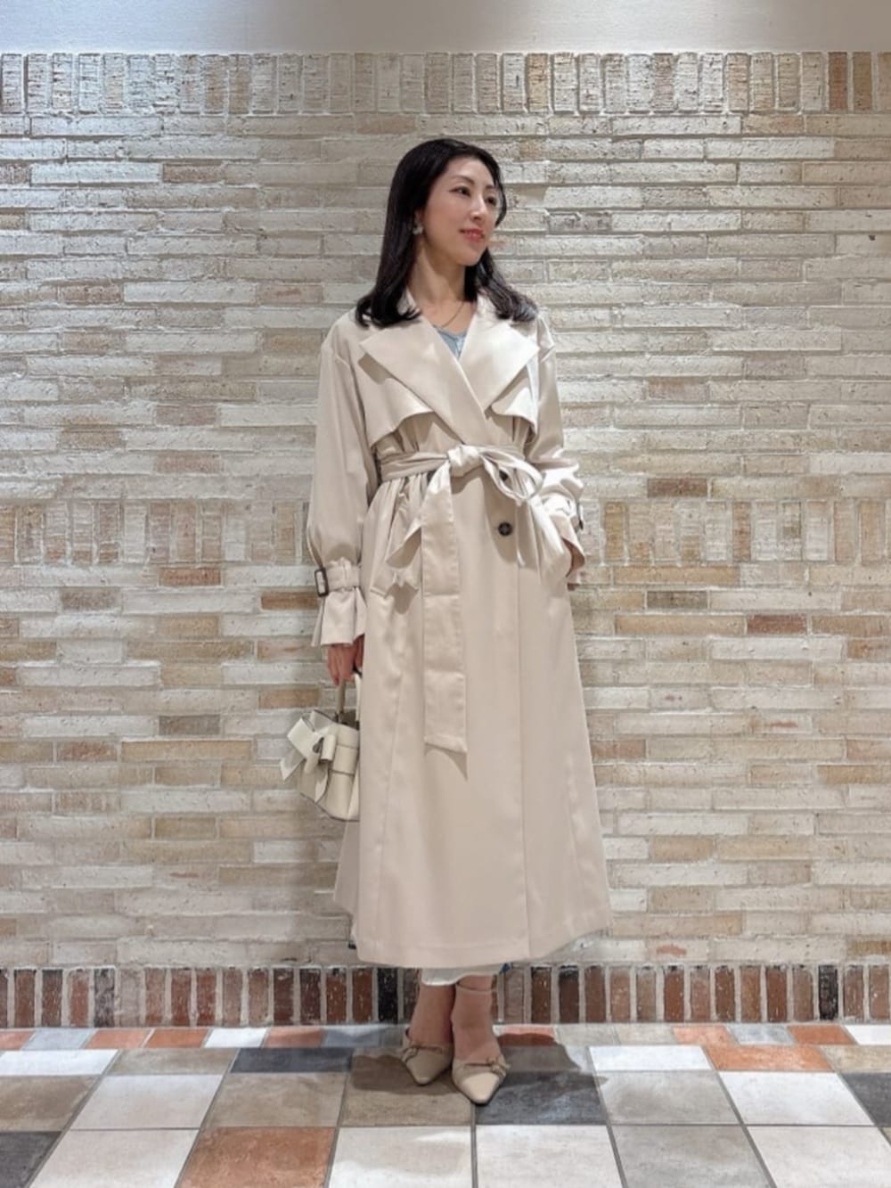 ホワイト系のショルダーバッグ、ベージュ系のトレンチコート、ベージュ系のパンプスを着用したレディースの冬コーディネートの2枚目の写真