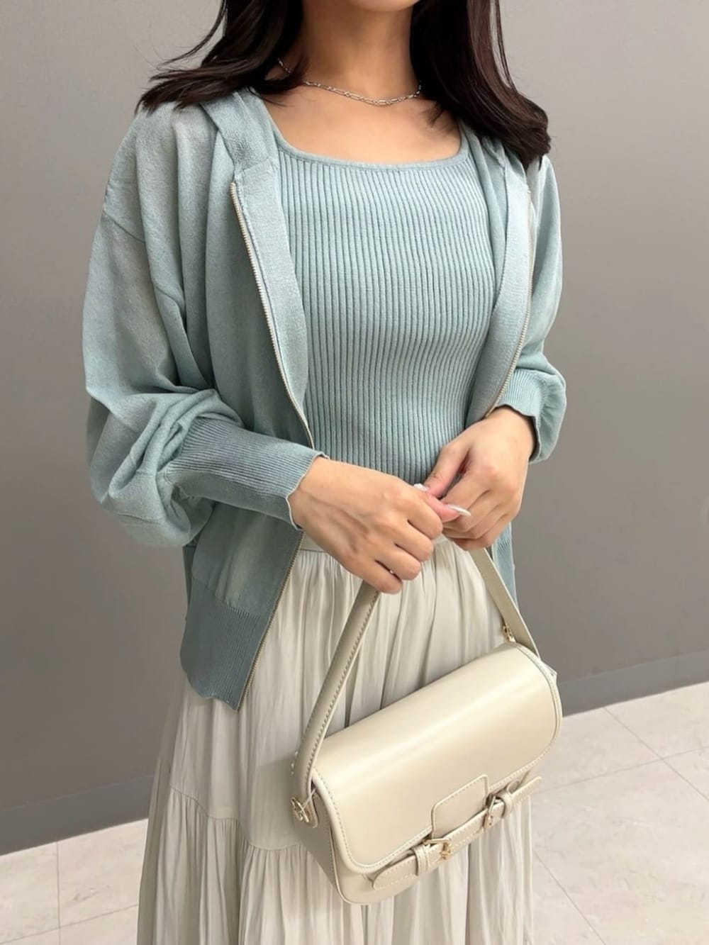 ホワイト系のショルダーバッグ、ホワイト系のスカート、グリーン系のパーカーを着用したレディースの夏コーディネートの3枚目の写真