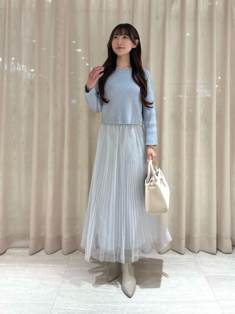 ホワイト系のショルダーバッグ、ブルー系のニット/セーター、グレー系のスカートを着用したレディースの冬コーディネートの2枚目の写真