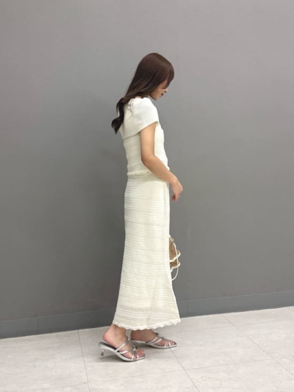 シルバー系のパンプス、ベージュ系のショルダーバッグ、ホワイト系のワンピースを着用したレディースの夏コーディネートの2枚目の写真