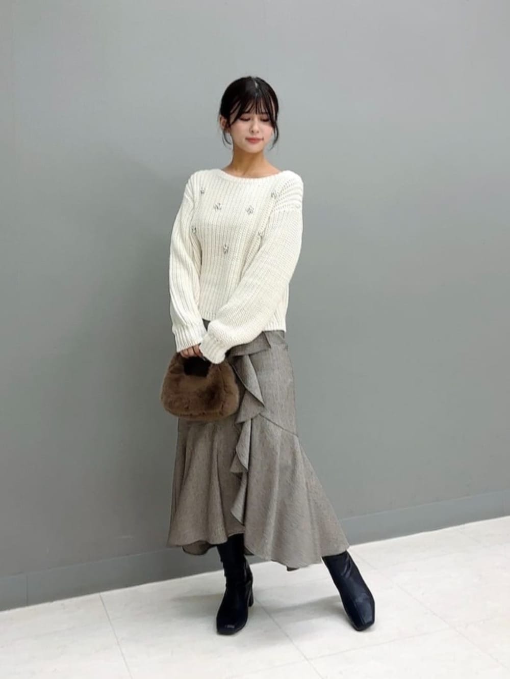 ブラウン系のハンドバッグ、ホワイト系のニット/セーター、ブラウン系のスカートを着用したレディースの冬コーディネートの2枚目の写真