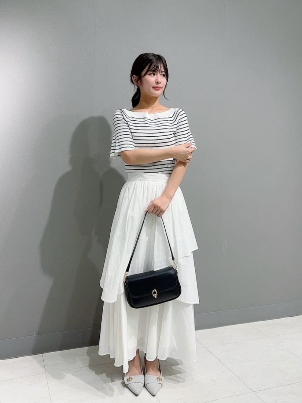 ブラック系のショルダーバッグ、ホワイト系のニット/セーター、ホワイト系のスカートを着用したレディースの春コーディネートの2枚目の写真