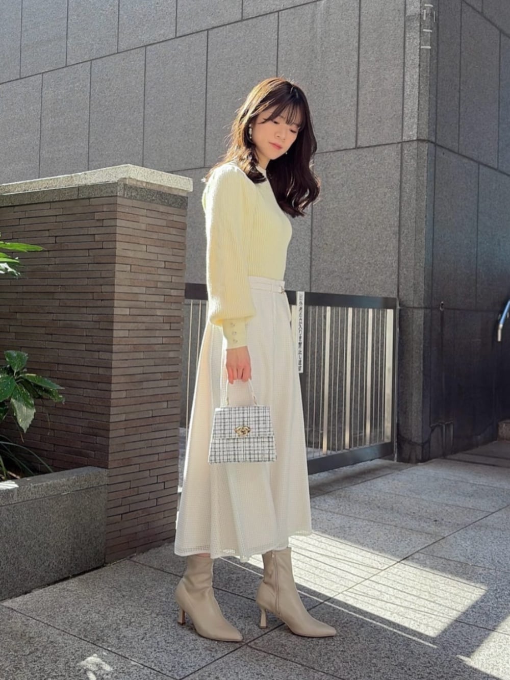 ホワイト系のショルダーバッグ、イエロー系のニット/セーター、ホワイト系のスカートを着用したレディースの冬コーディネートの2枚目の写真