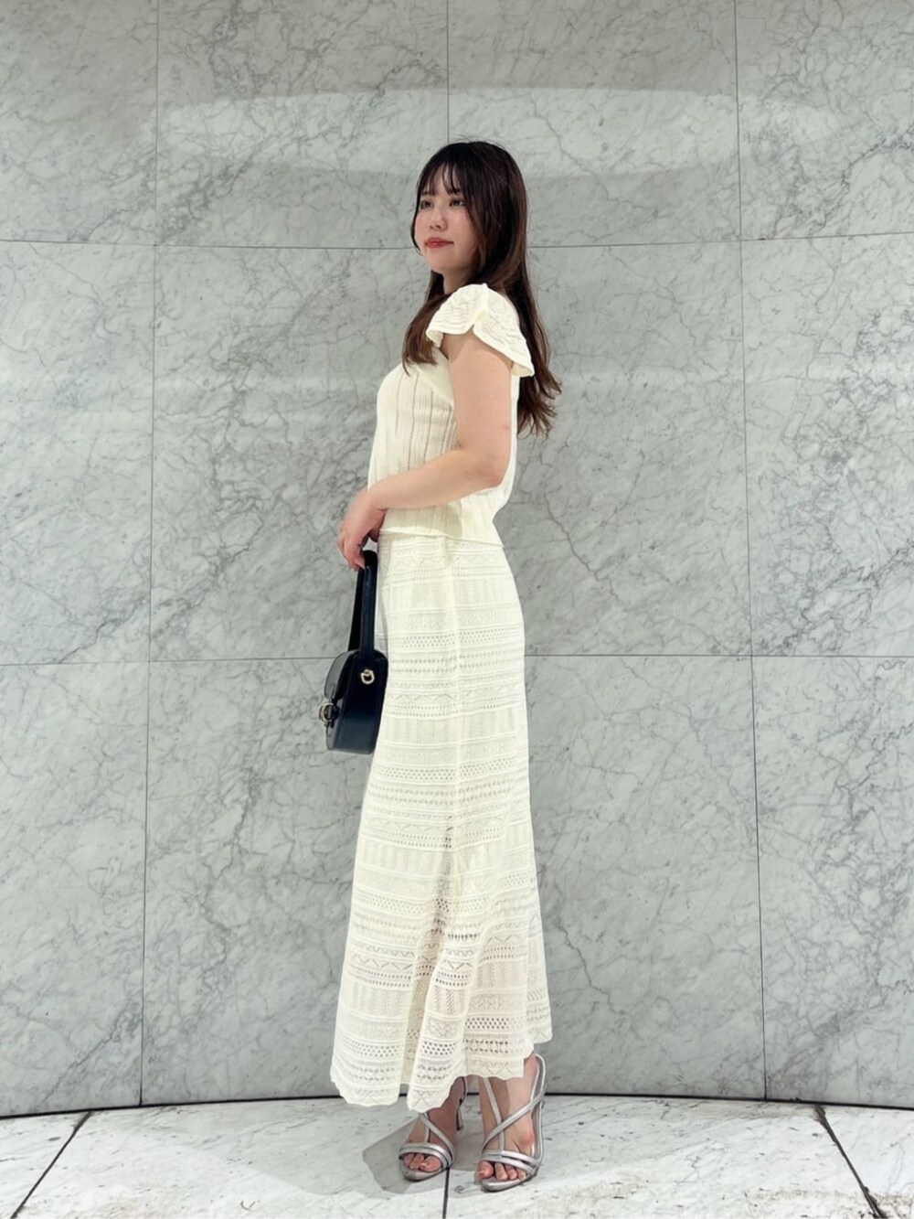 シルバー系のパンプス、ブラック系のショルダーバッグ、ホワイト系のワンピースを着用したレディースの夏コーディネートの3枚目の写真