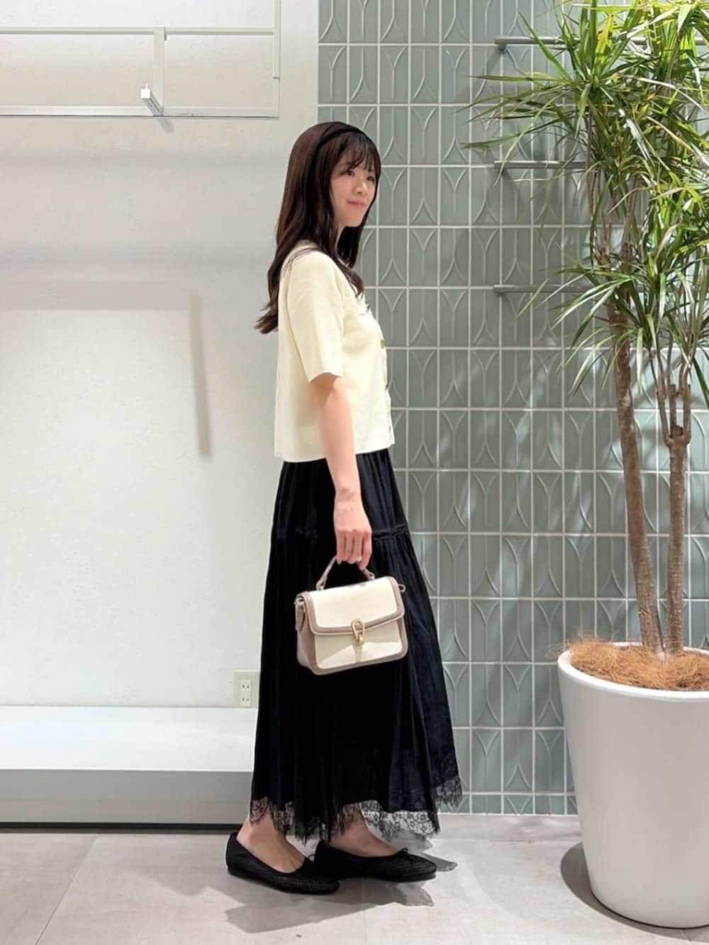 グレー系のショルダーバッグ、ホワイト系のカーディガン/ボレロ、ブラック系のスカートを着用したレディースの秋コーディネートの2枚目の写真