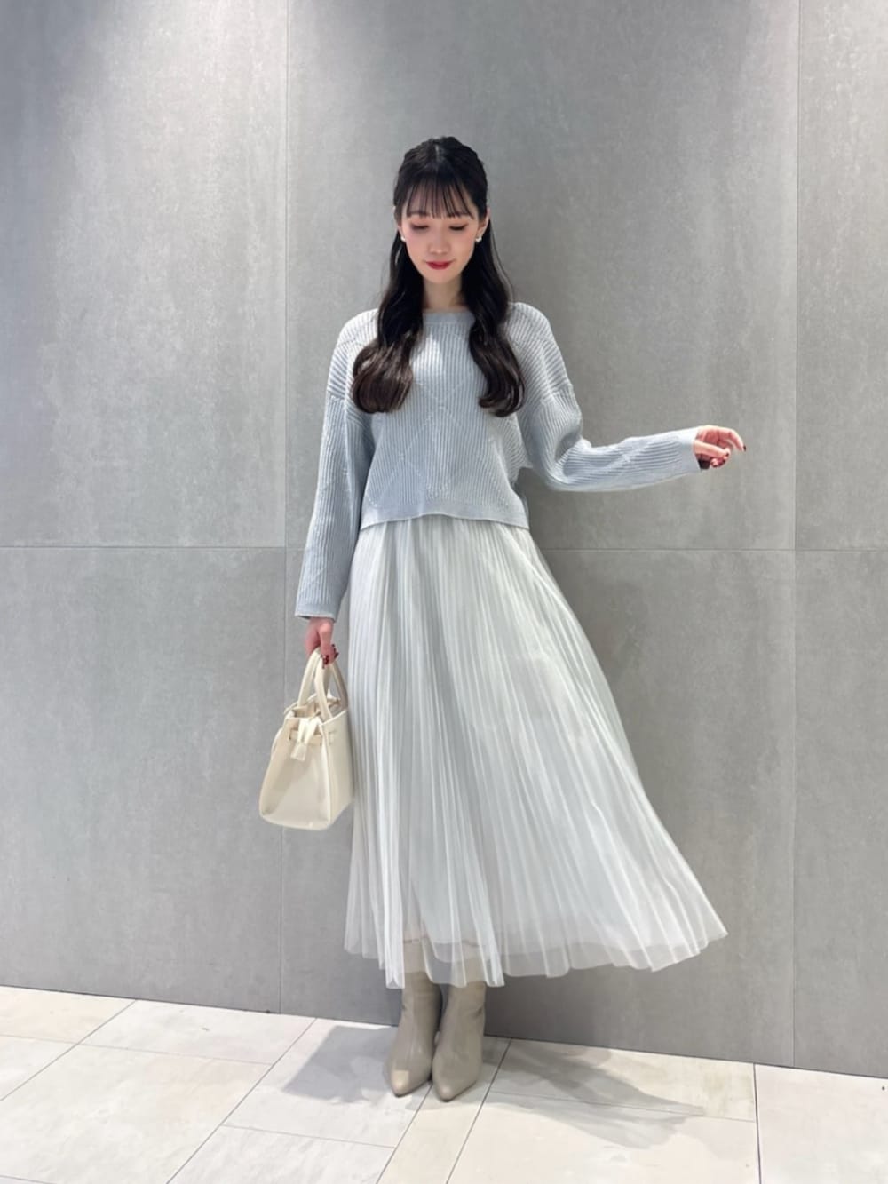 ホワイト系のショルダーバッグ、ブルー系のニット/セーター、グレー系のスカートを着用したレディースの春コーディネートの2枚目の写真
